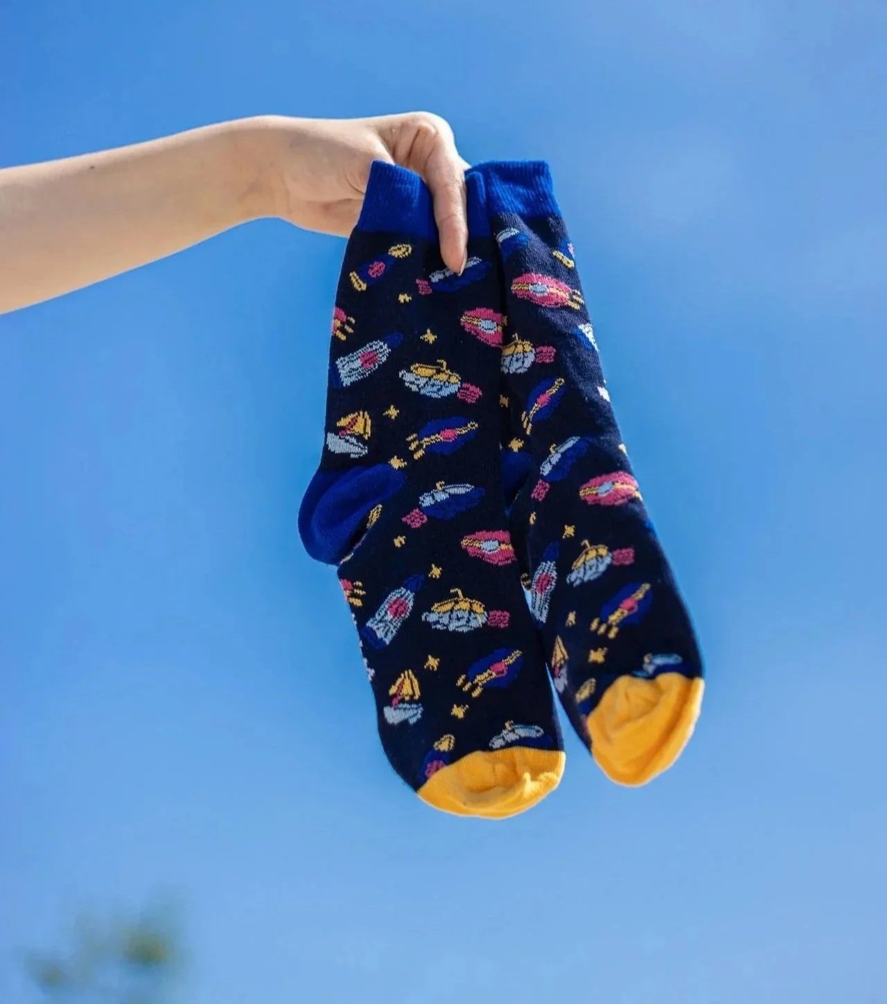 Hand houdt een paar sokken met een ruimtevaartmotief tegen een blauwe lucht.