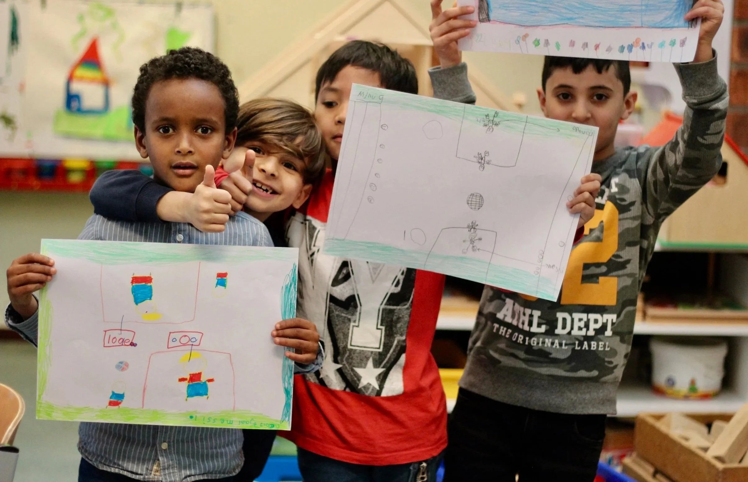 Vier kinderen in een klaslokaal tonen handgetekende tekeningen van een sportveld.
