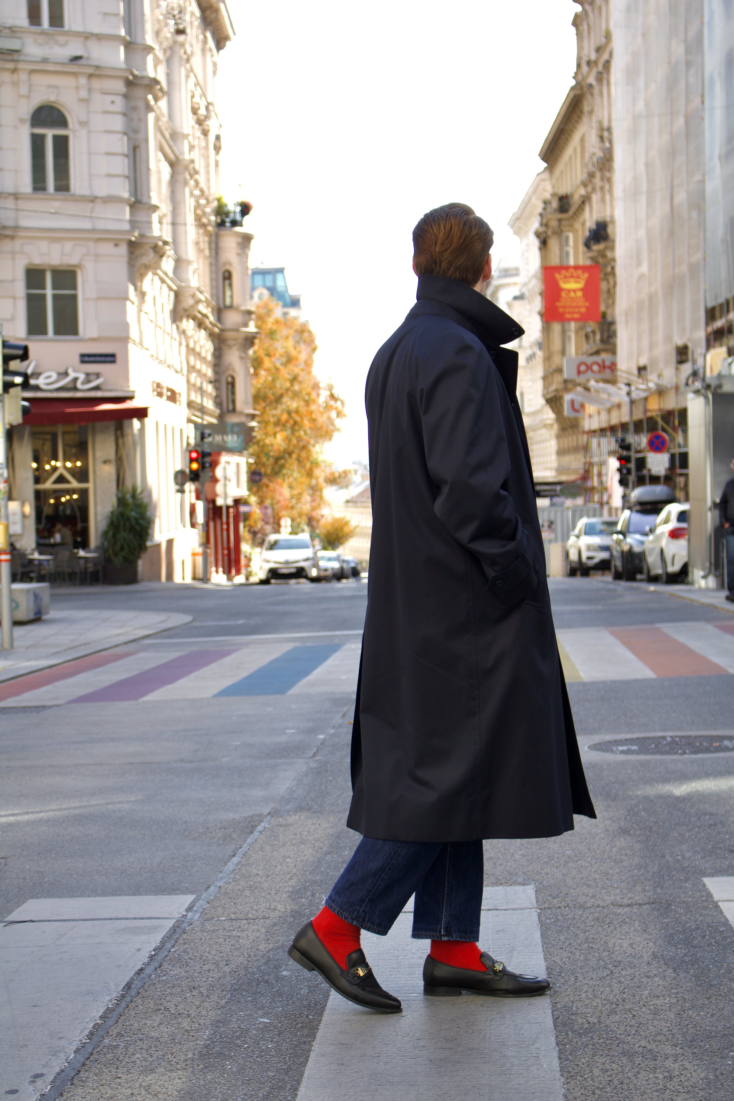 A person in a black coat and red socks walking across a city crosswalk.