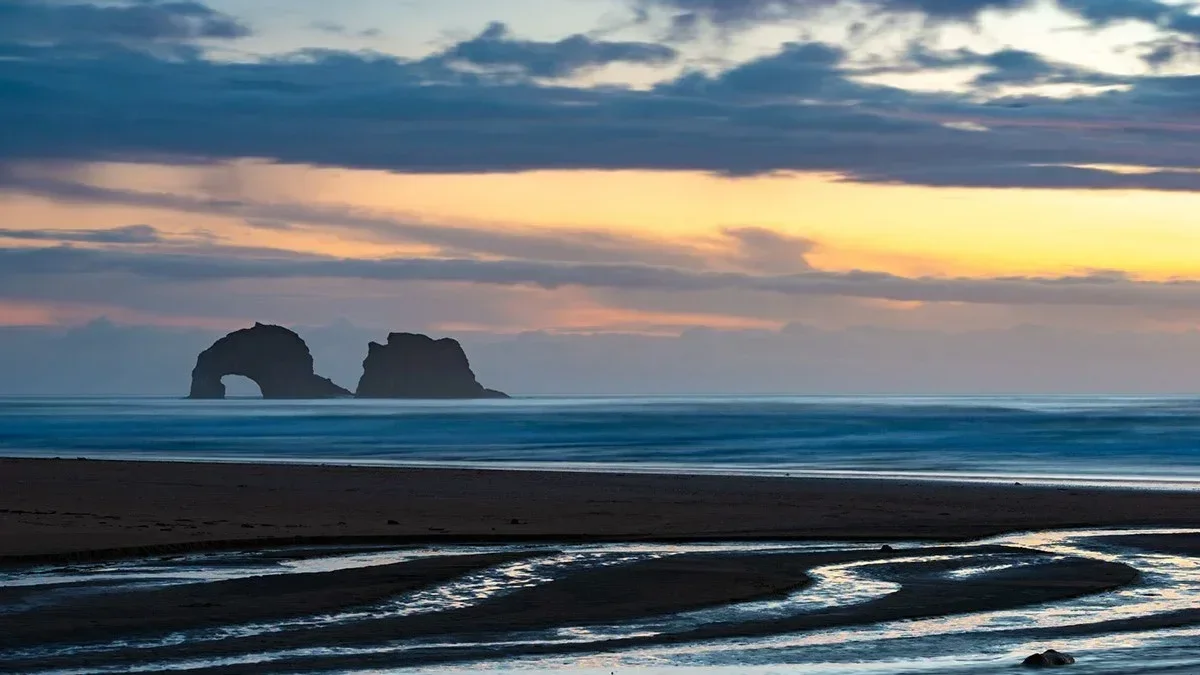 Sunset over a beach with rock formations in the distance and the tide coming in.