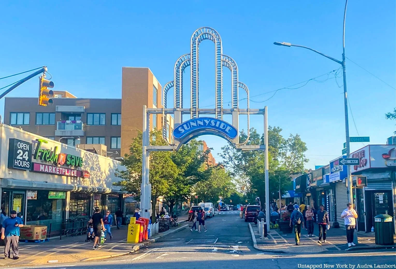 Street scene at Sunnyside with people walking, storefronts, and a sign arching over the street that reads 'Sunnyside.'