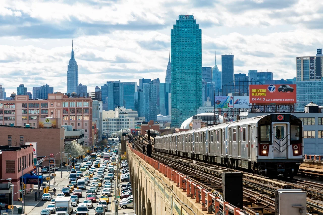 A cityscape featuring a train on elevated tracks with skyscrapers and a busy street below filled with cars.
