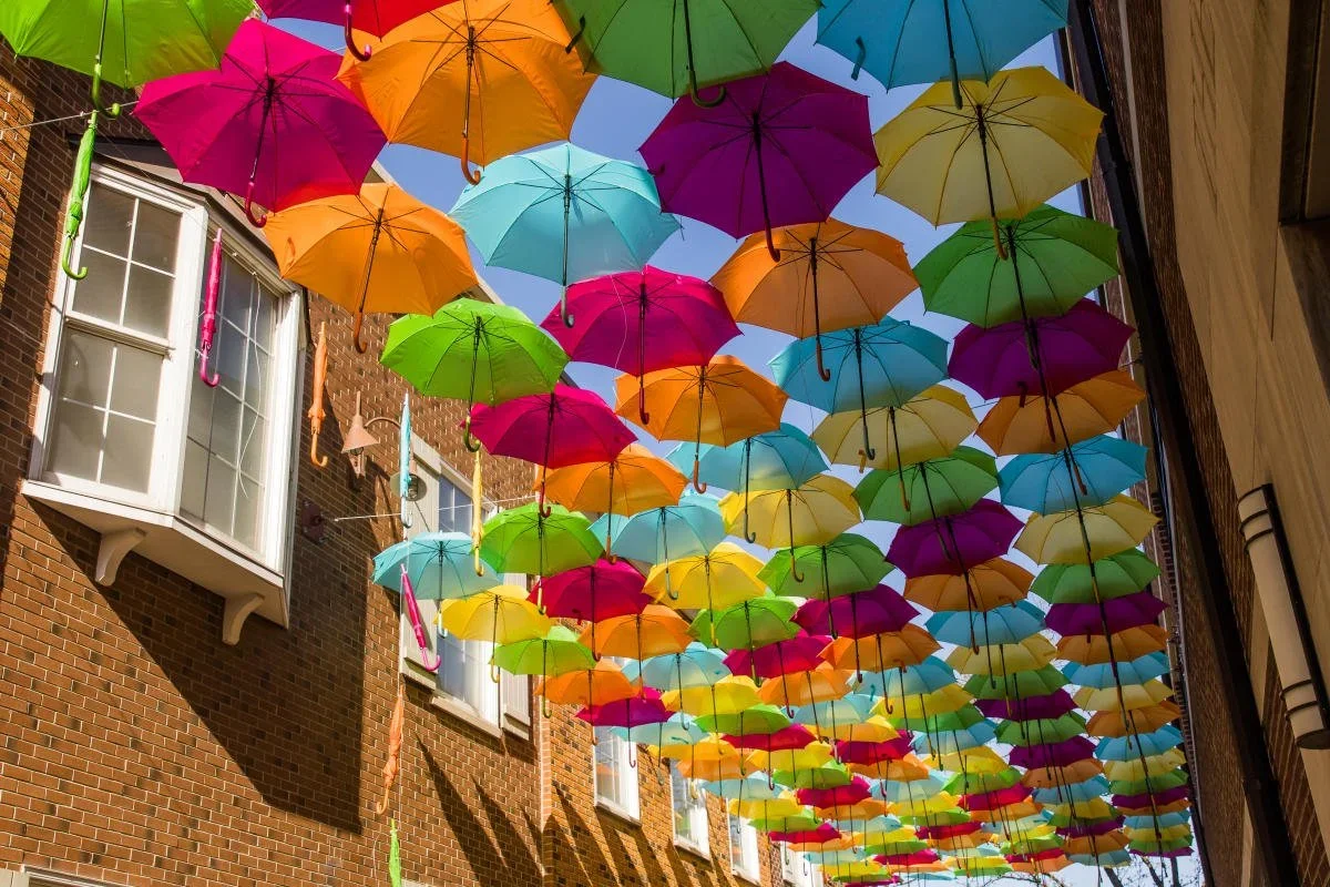 Colorful umbrellas hanging overhead in an outdoor city street with brick buildings.