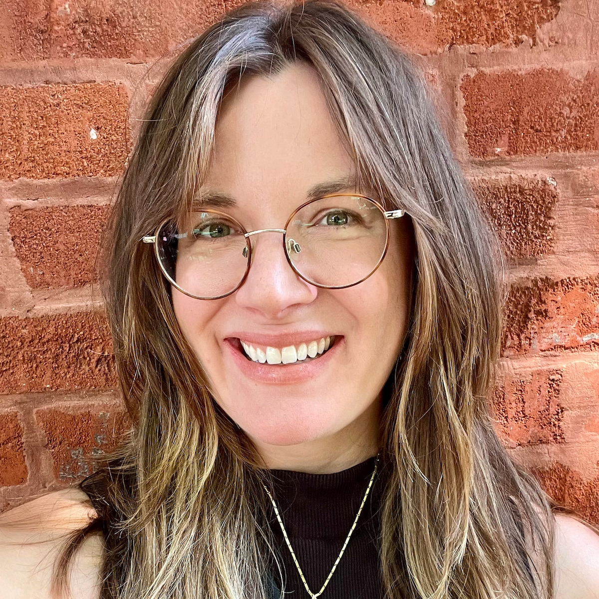 headshot of Gemma Petrie, a white woman with long brown hair and glasses. She smiles and wears a black top with a necklace. 
