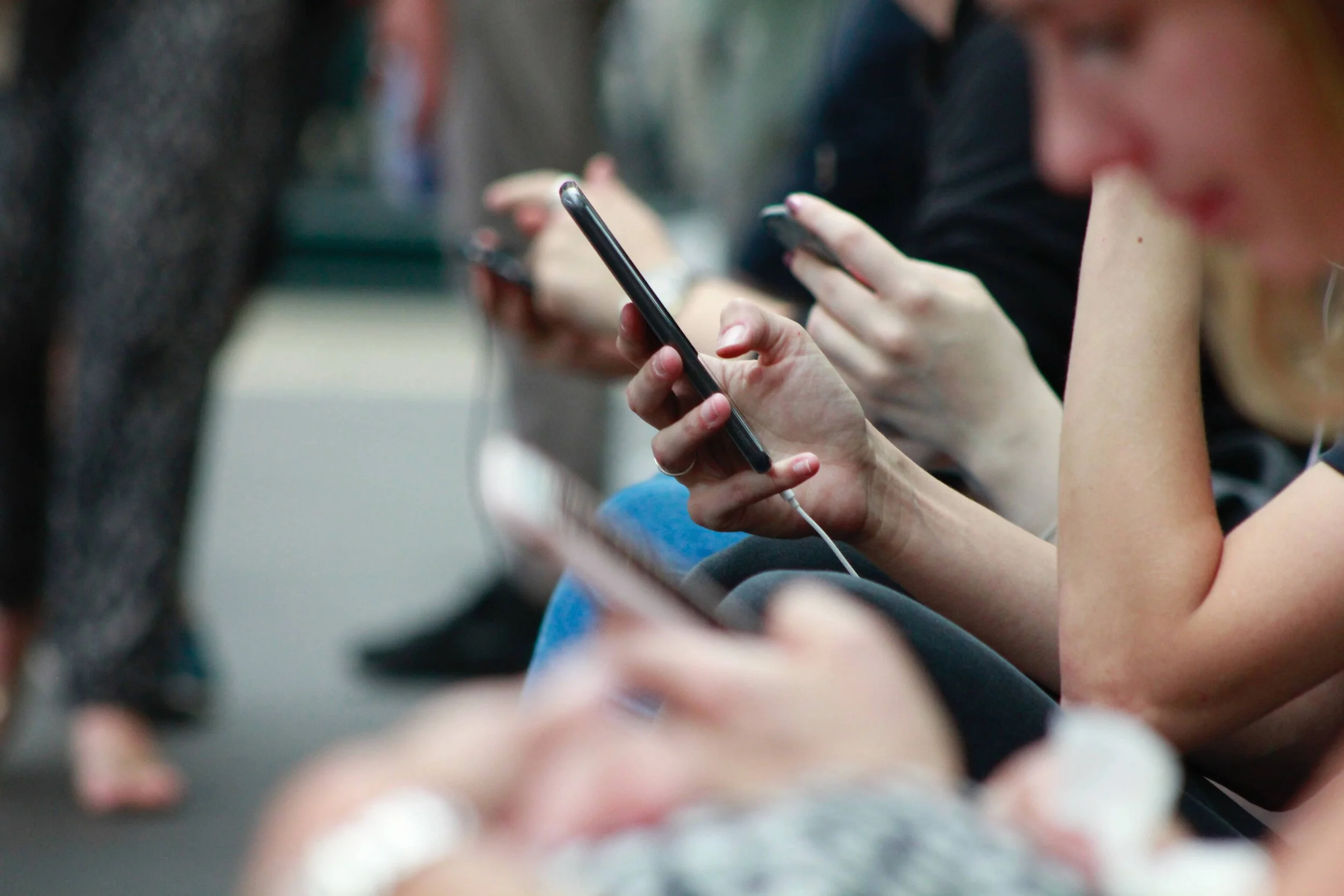 The hands of many people scrolling their phones, checking email or social media instead of working on their website copywriting.