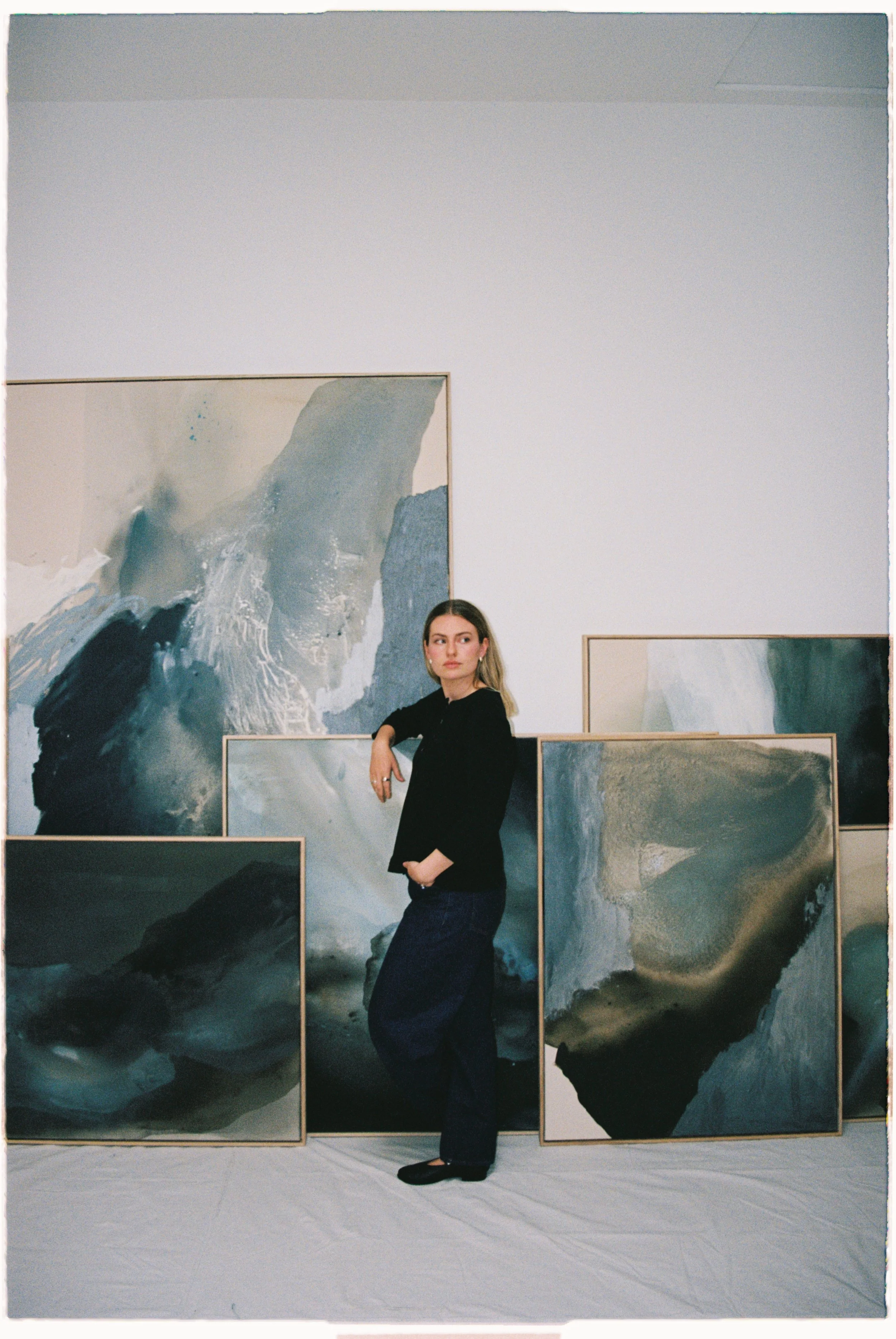 A woman standing in an art gallery, surrounded by abstract paintings with shades of blue, gray, and black.