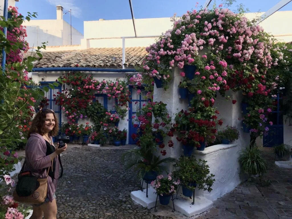 Karen holding a camera, smiling, in a traditional flower filled cordobese patio