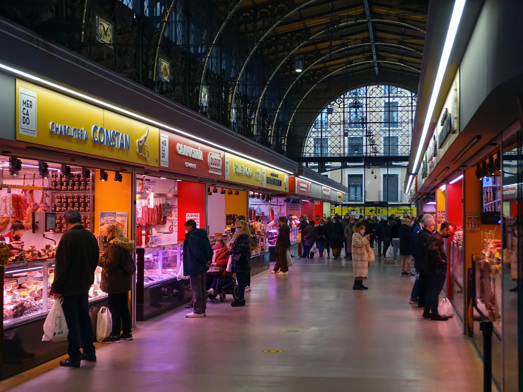 Shoppers browse a vibrant Zaragoza market, surrounded by an array of fresh produce and diverse food options.