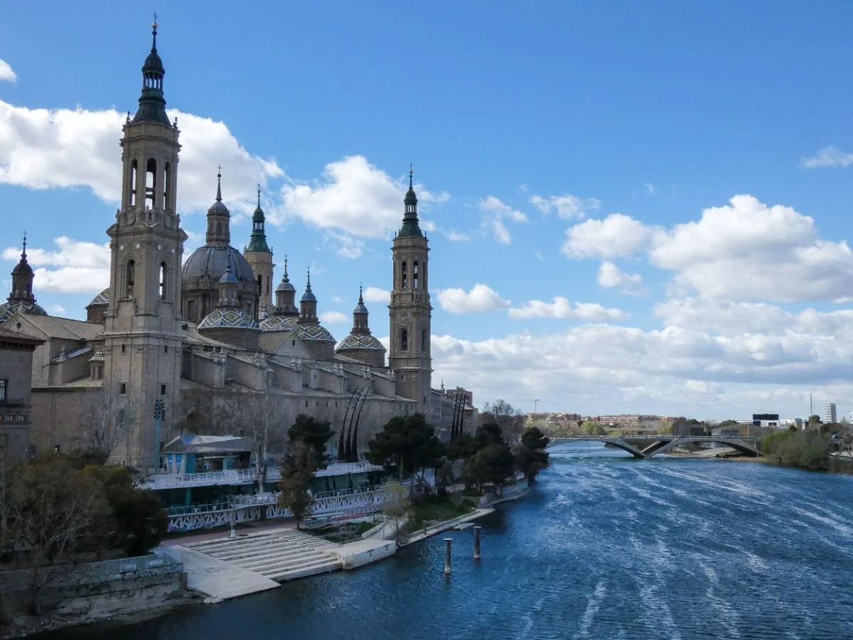 A tranquil river scene with a bridge and a beautiful cathedral in the distance, capturing the charm of Zaragoza, Spain.
