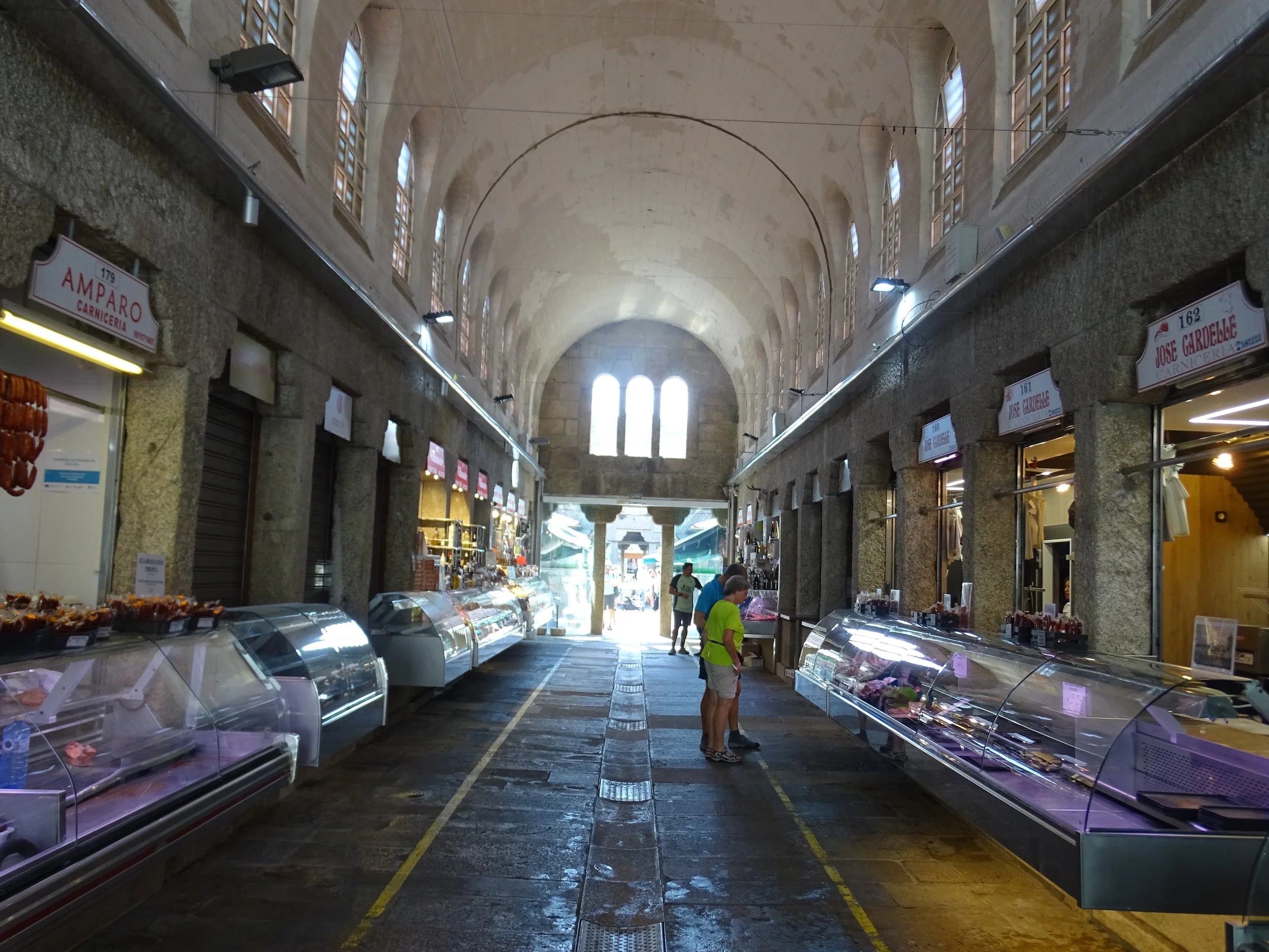 A bustling aisle lined with diverse food items, highlighting the stone architecture of Santiago de Compostela's Mercado de Abastos.