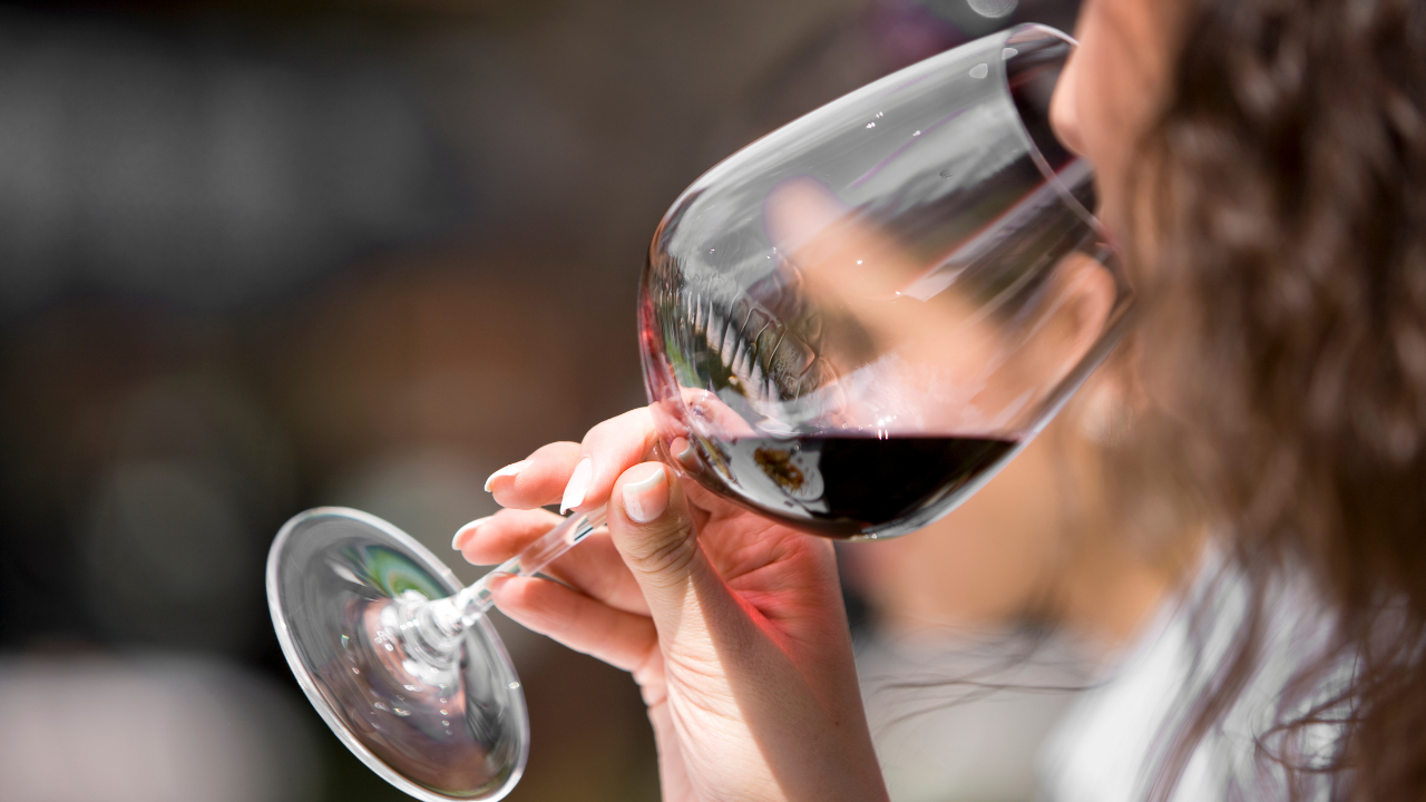 Person with curly hair drinking red wine from a glass outdoors.