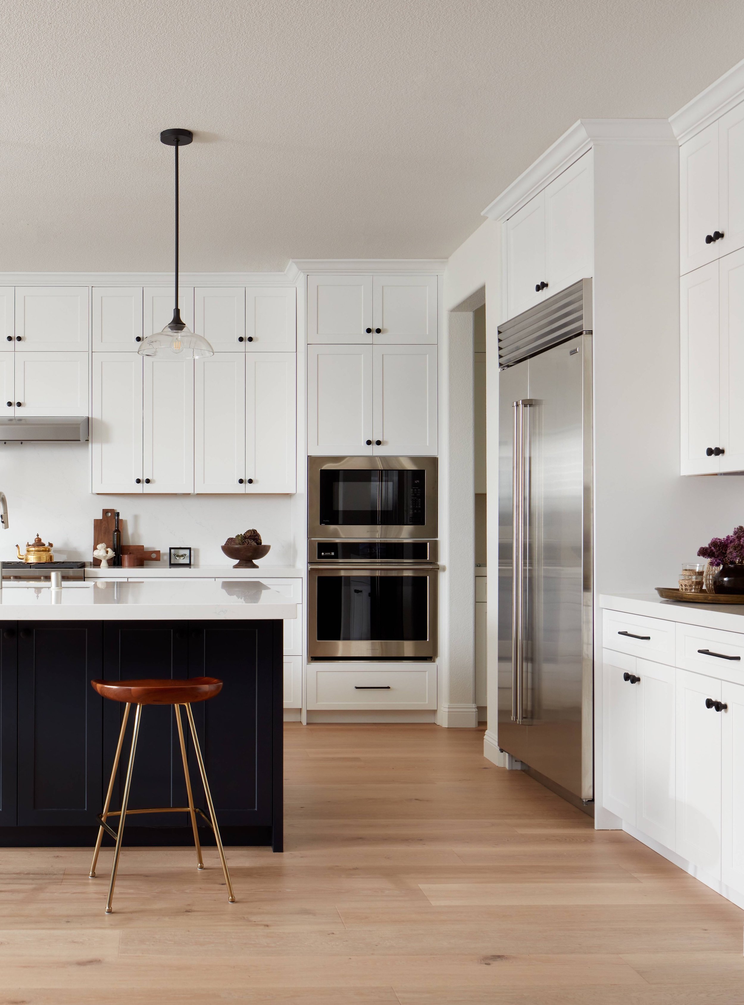 Modern kitchen with white cabinets, stainless steel appliances, a black kitchen island with a wooden stool, and light wood flooring.