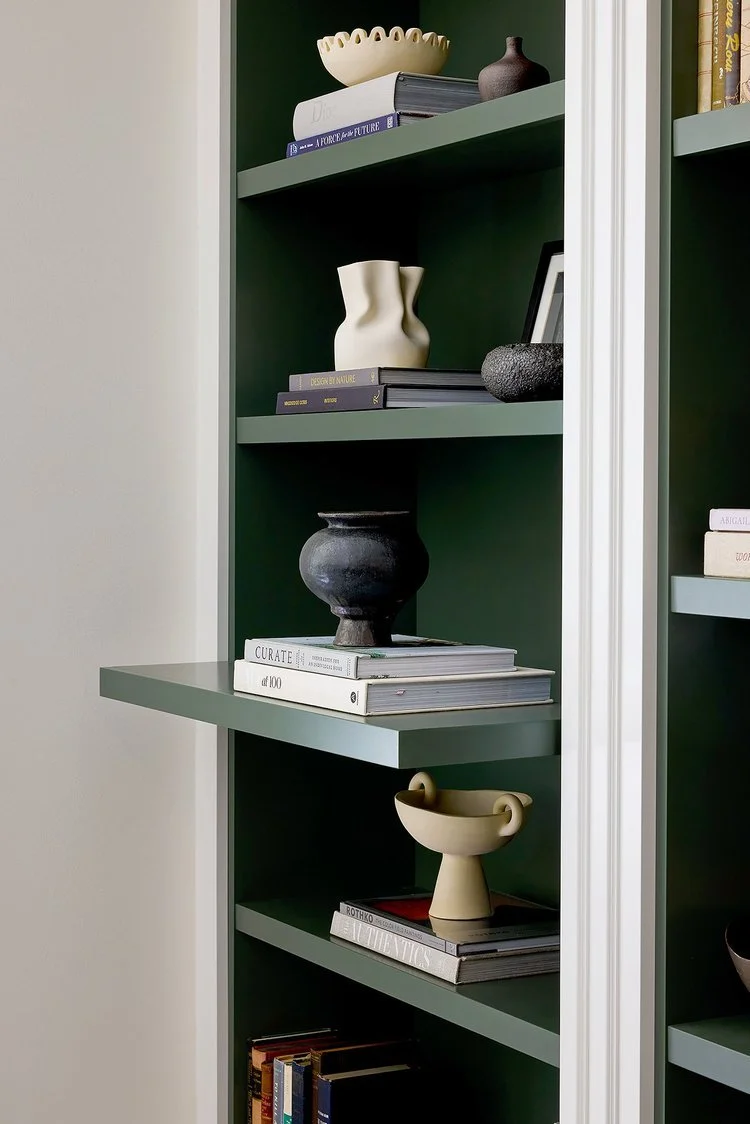 Decorative vases and books arranged on green wall-mounted shelves.