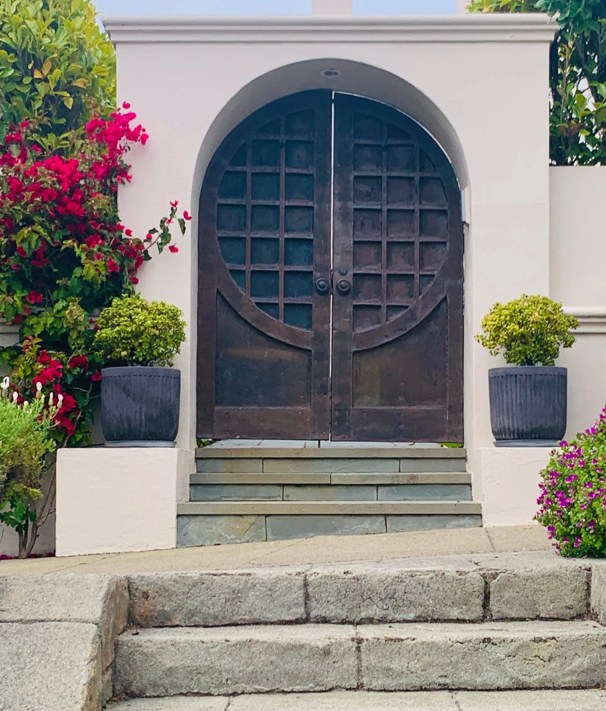 unique custom, heavy timber arched exterior double doors that mimic an aged bronze or metal patina, arched wood doors with distinct grid layout.