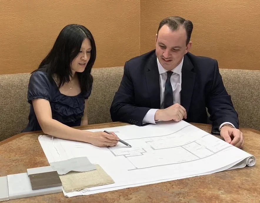 A woman and a man in business attire sitting at a table reviewing architectural plans.