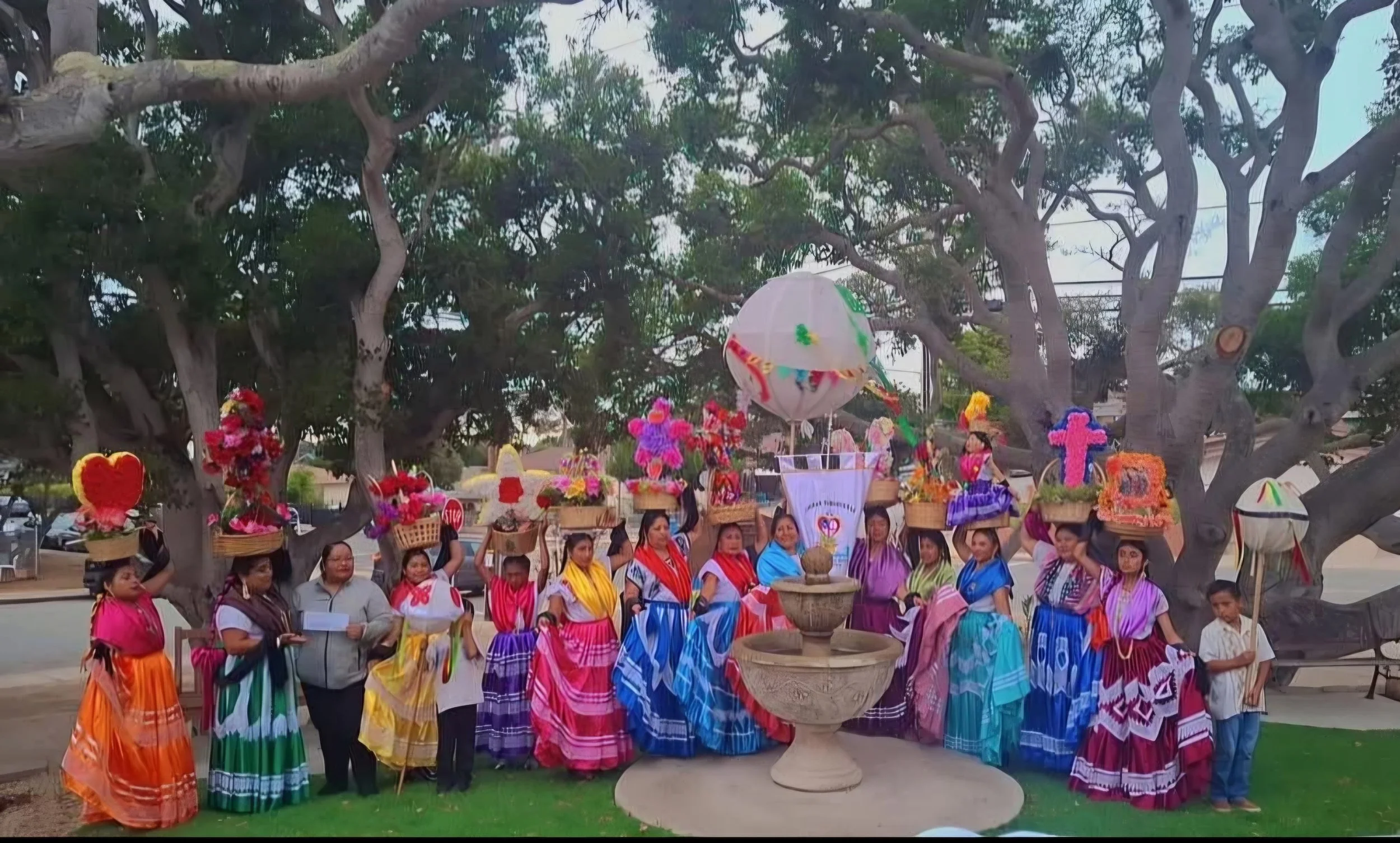 Large group of performers in colorful outfits with large trees in the background