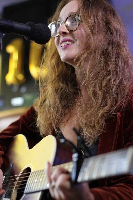 Photo of Lady Smiling looking sideways wearing glasses with long hair. in front of microphone.