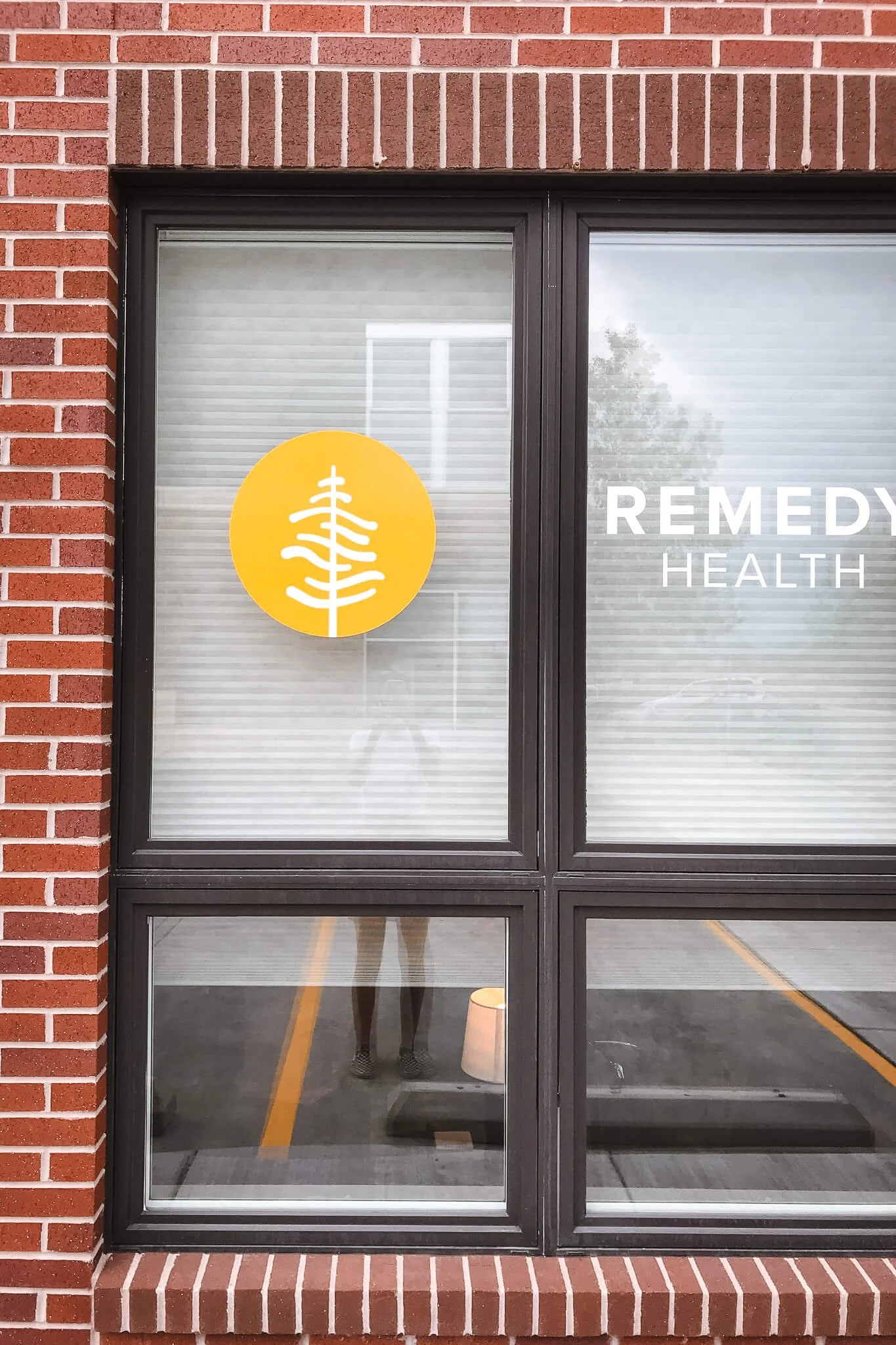Minimalist circular window graphic with a modern tree icon for Remedy Health in Bozeman, MT, paired with a clean vinyl text application on frosted windows].