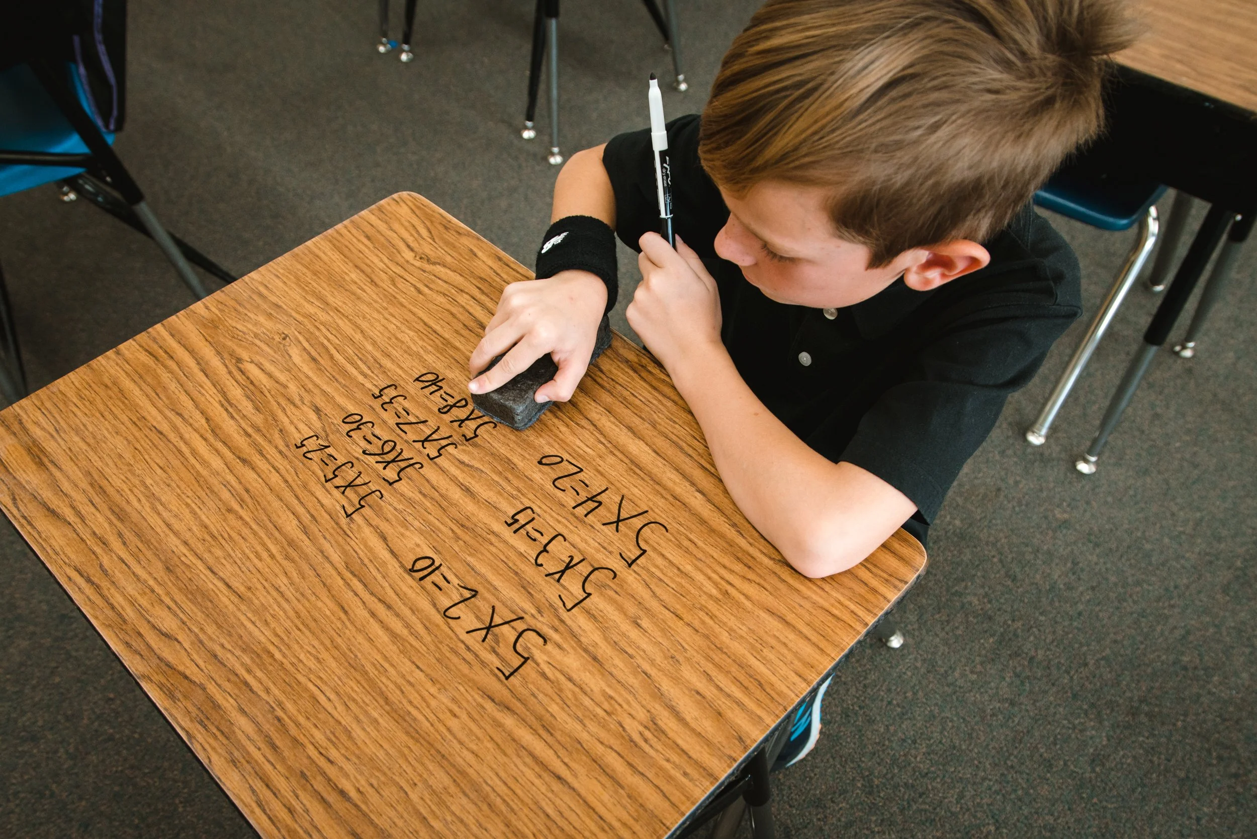 Student using a rectangular eraser to remove marker from a clear dry erase desk covering.