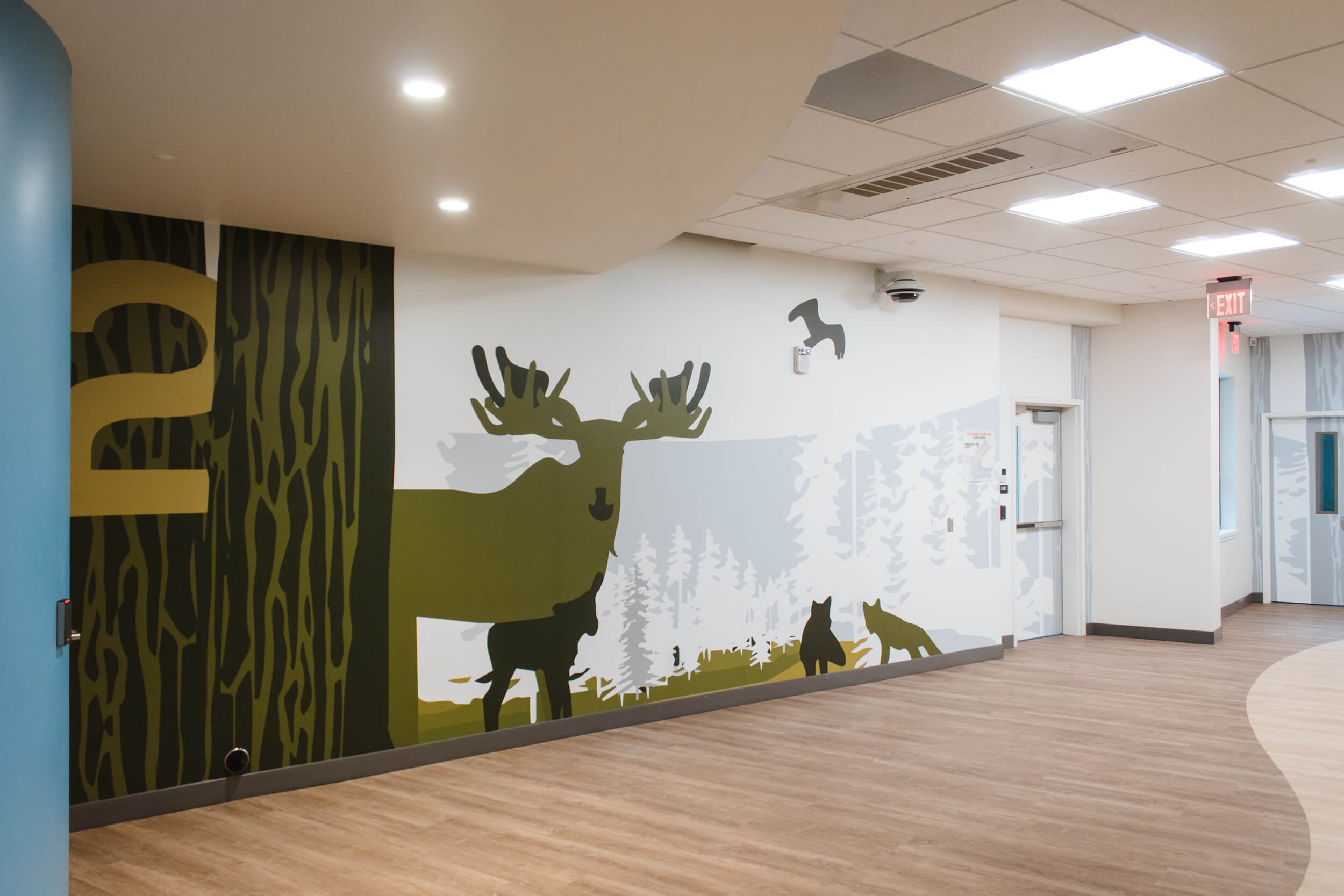 Nature-themed vinyl wall wrap in a hospital or medical corridor, featuring illustrated moose, trees, and wildlife with calming earth tones – installed at Shodair Children’s Hospital in Helena, MT.