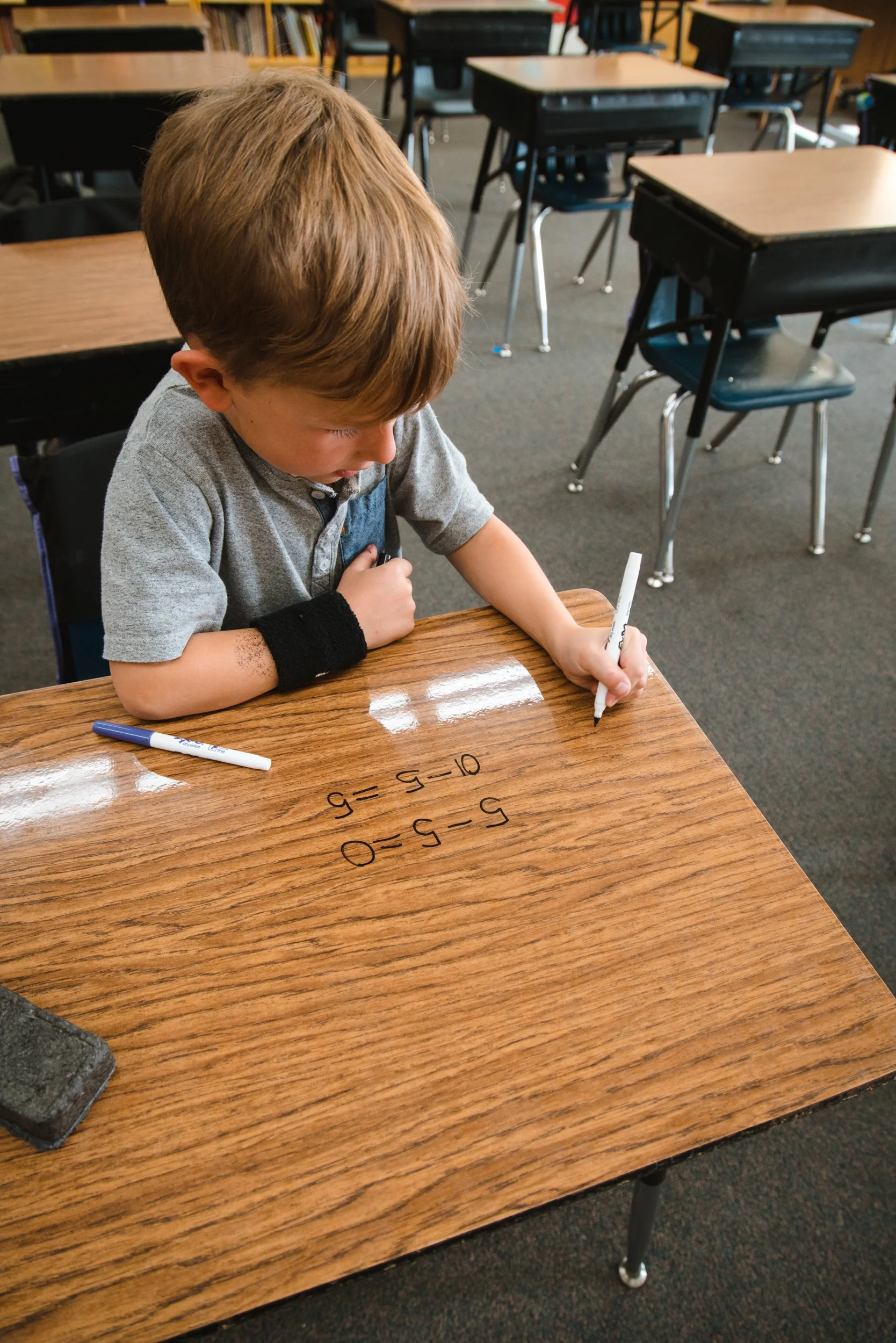 Angled view of a student working through math equations on a woodgrain dry erase desk.