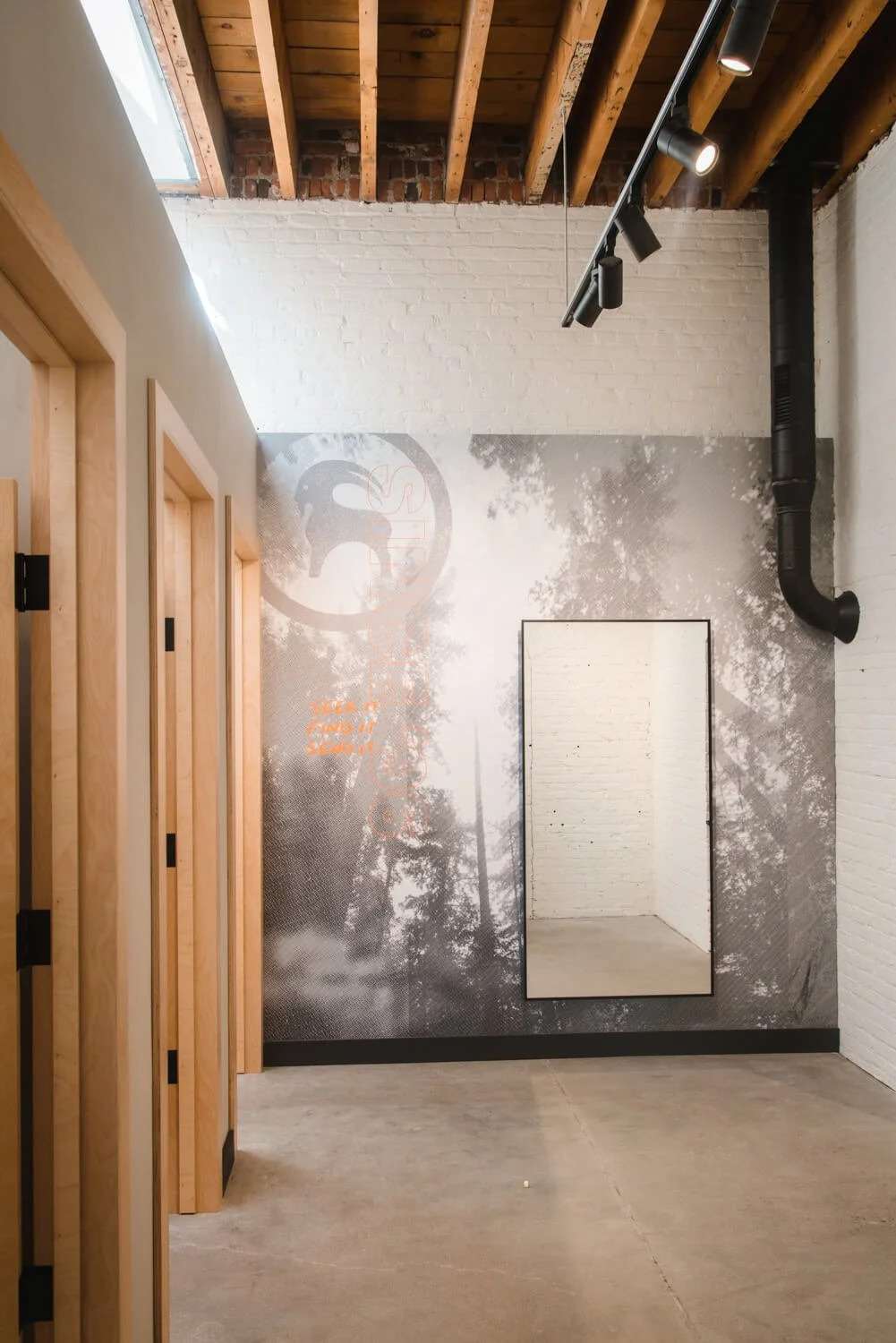 Grayscale forest wall wrap with the Sitka logo and motivational text, used to elevate an industrial retail interior near a fitting room area at Backcountry in Bozeman, MT.