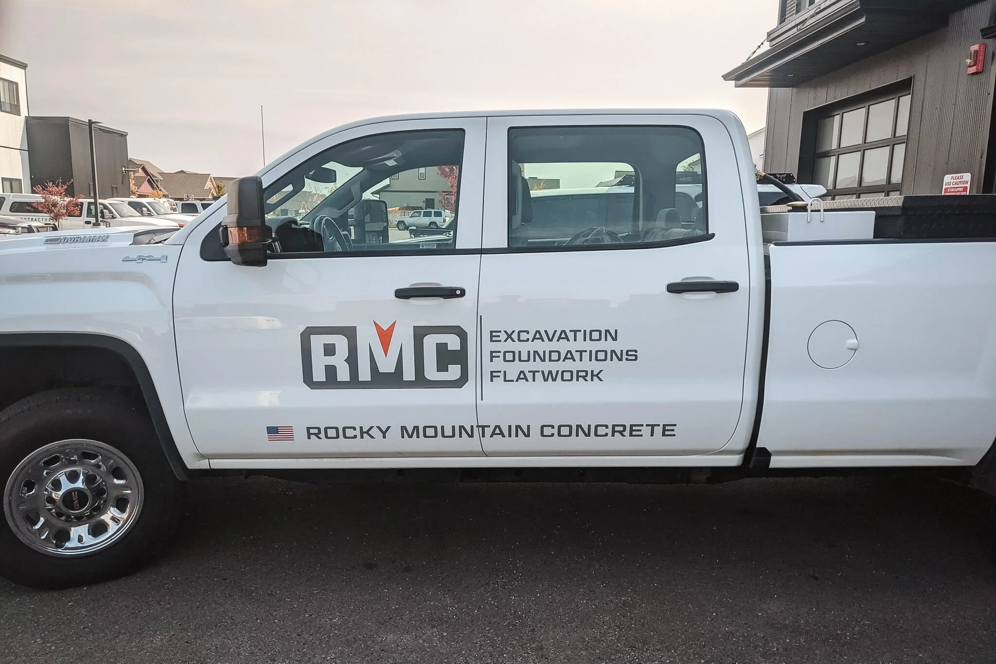 White pickup truck wrapped for Rocky Mountain Concrete (RMC) with gray and orange logo and typography highlighting excavation and flatwork services—a professional vinyl wrap for service vehicles in Bozeman, Montana.