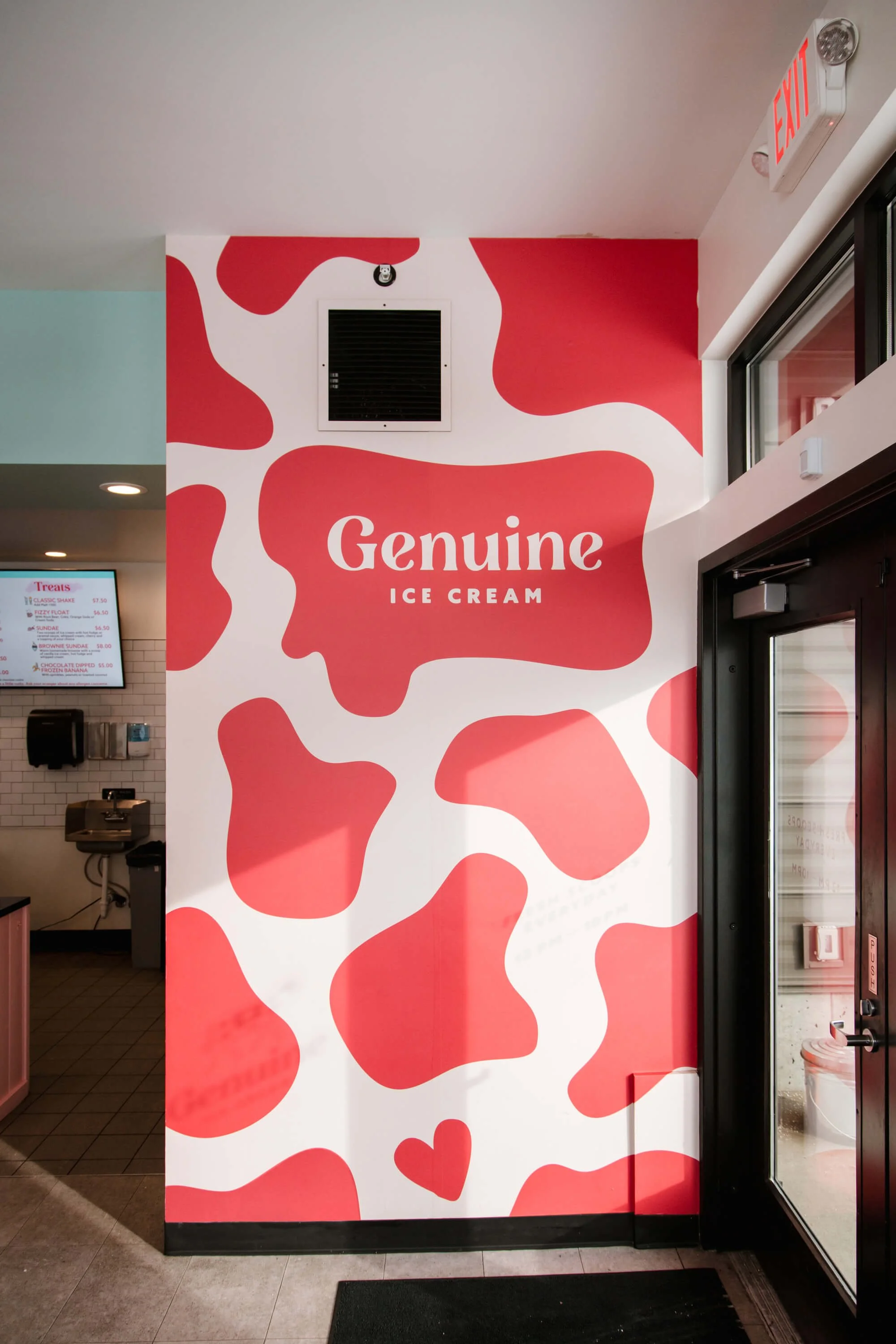 Bright red and white branded wall wrap with abstract cow print and "Genuine Ice Cream" logo in a fun, welcoming ice cream shop entrance. Installed by The Wrap Agency in Bozeman, MT.