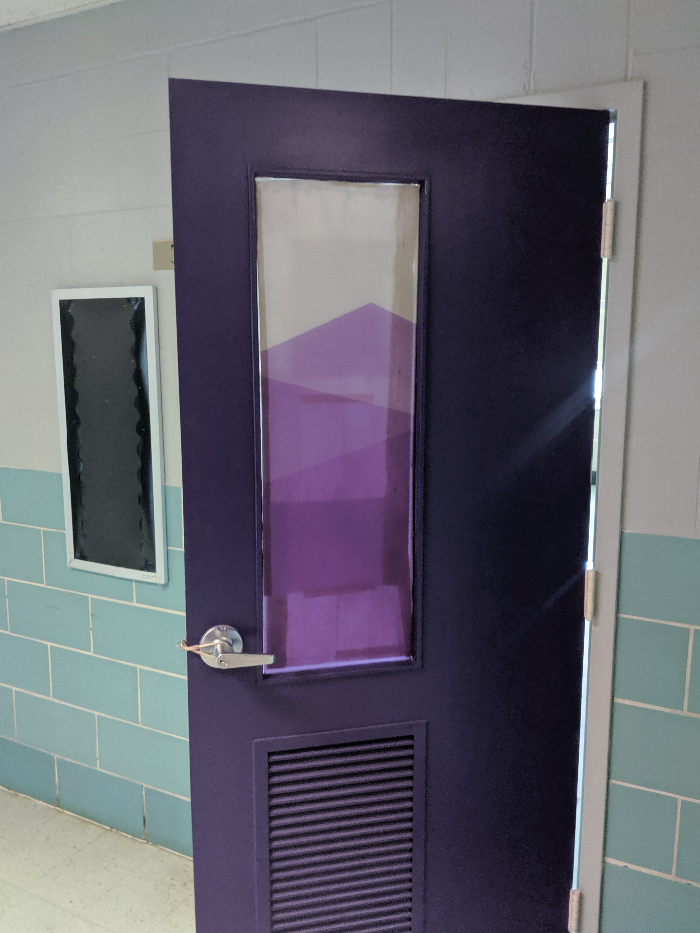 Purple door with window and frosted privacy film on the window in a hallway with teal tile walls. In Butte, Montana.