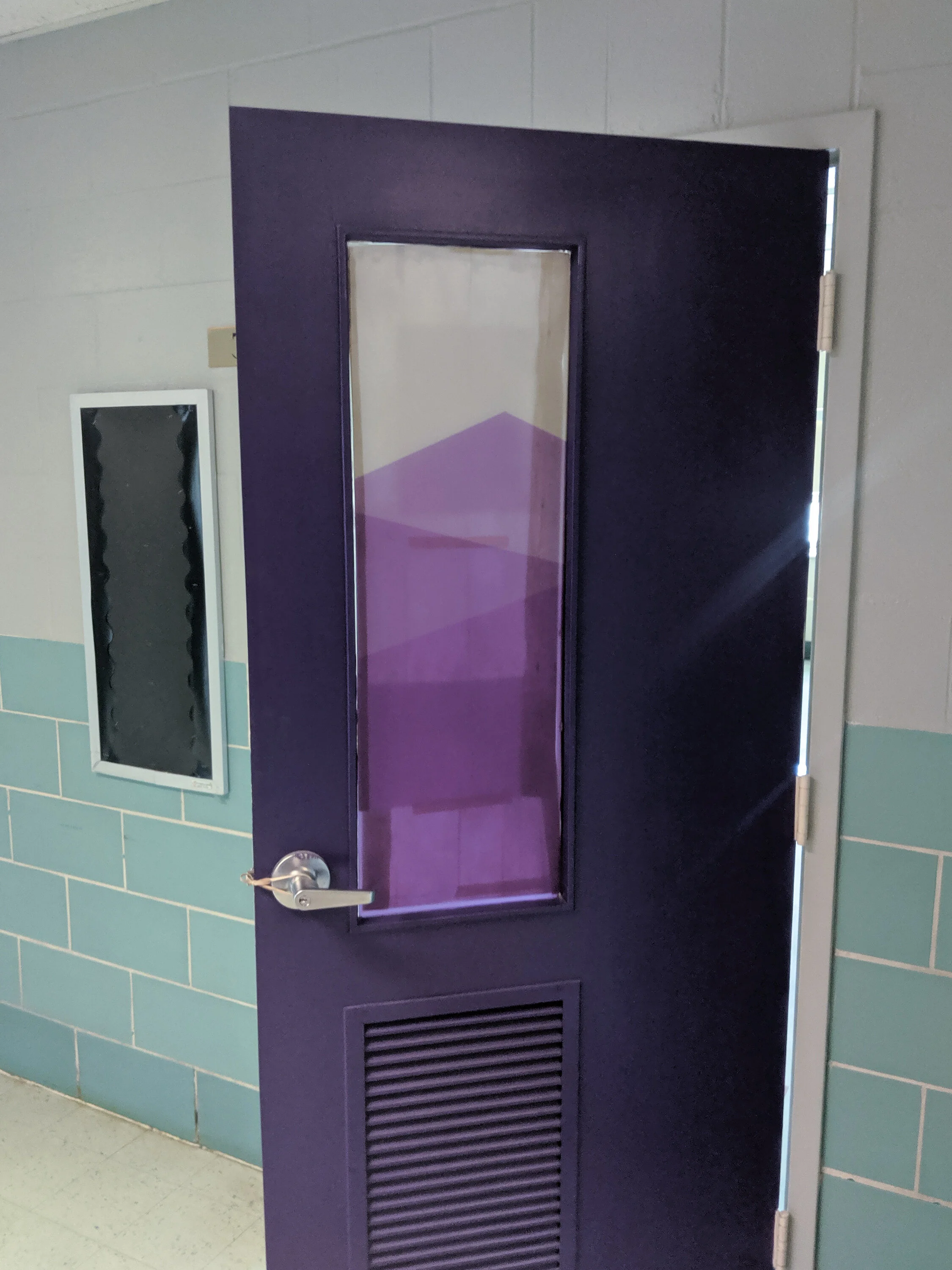 Purple door with window and frosted privacy film on the window in a hallway with teal tile walls. In Butte, Montana.