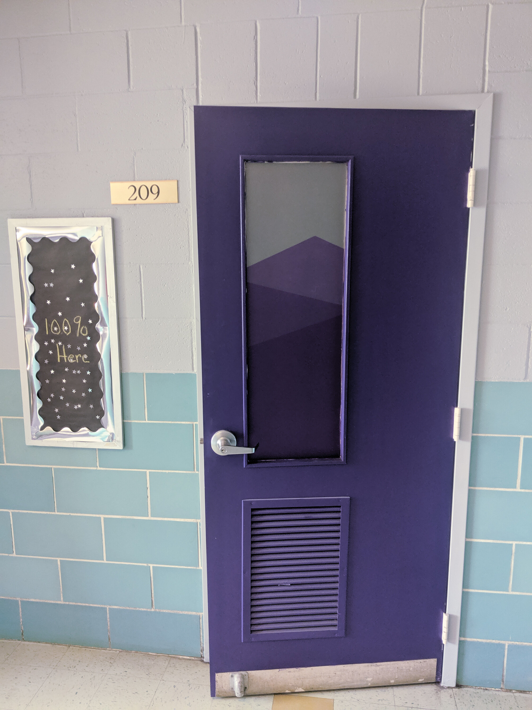 Purple classroom door marked "209" with window frosted privacy film. In Butte, Montana.
