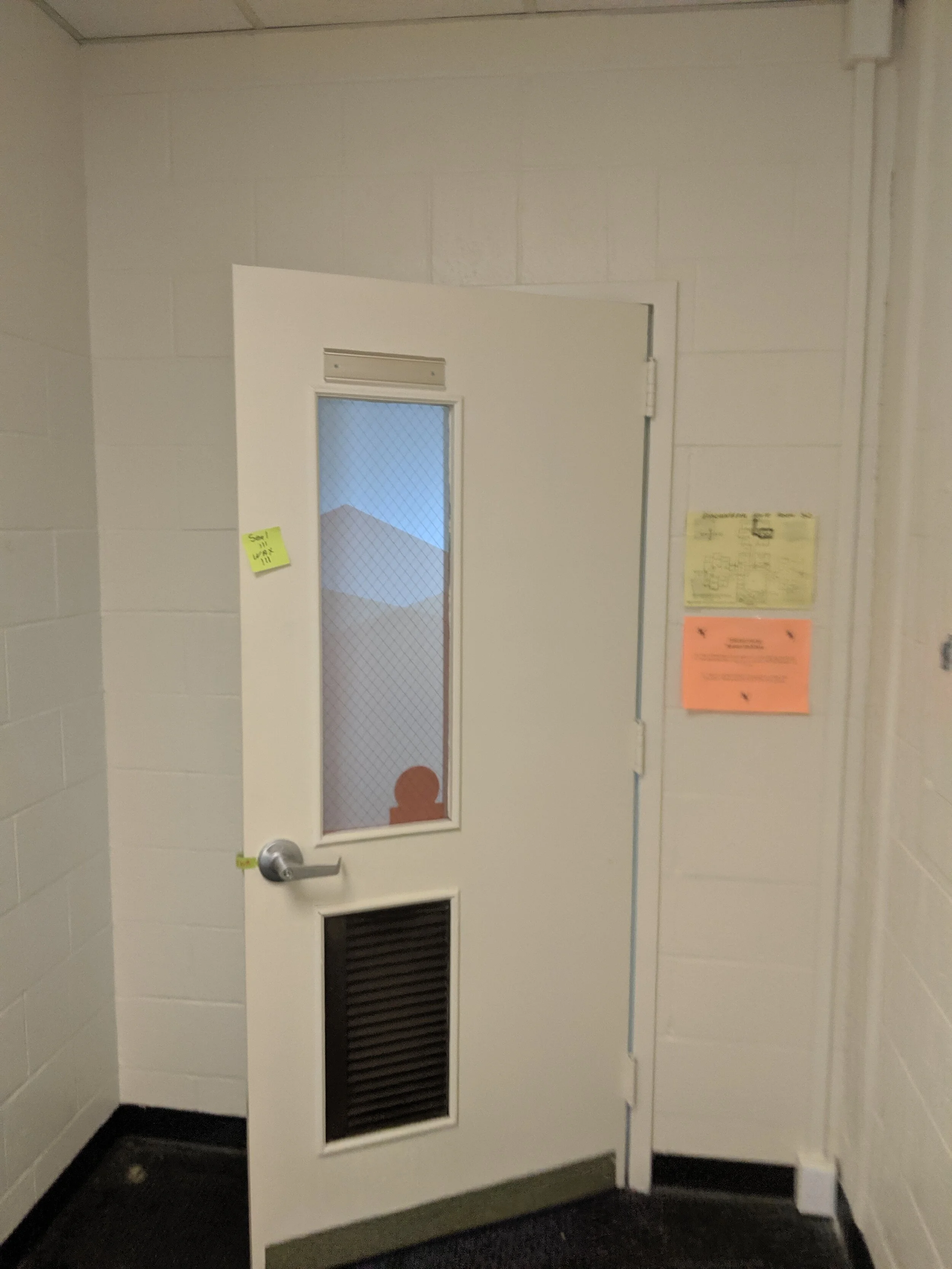 White door with a window and vent, post-it note on door, papers on wall. Frosted privacy vinyl on window. In Butte, Montana.