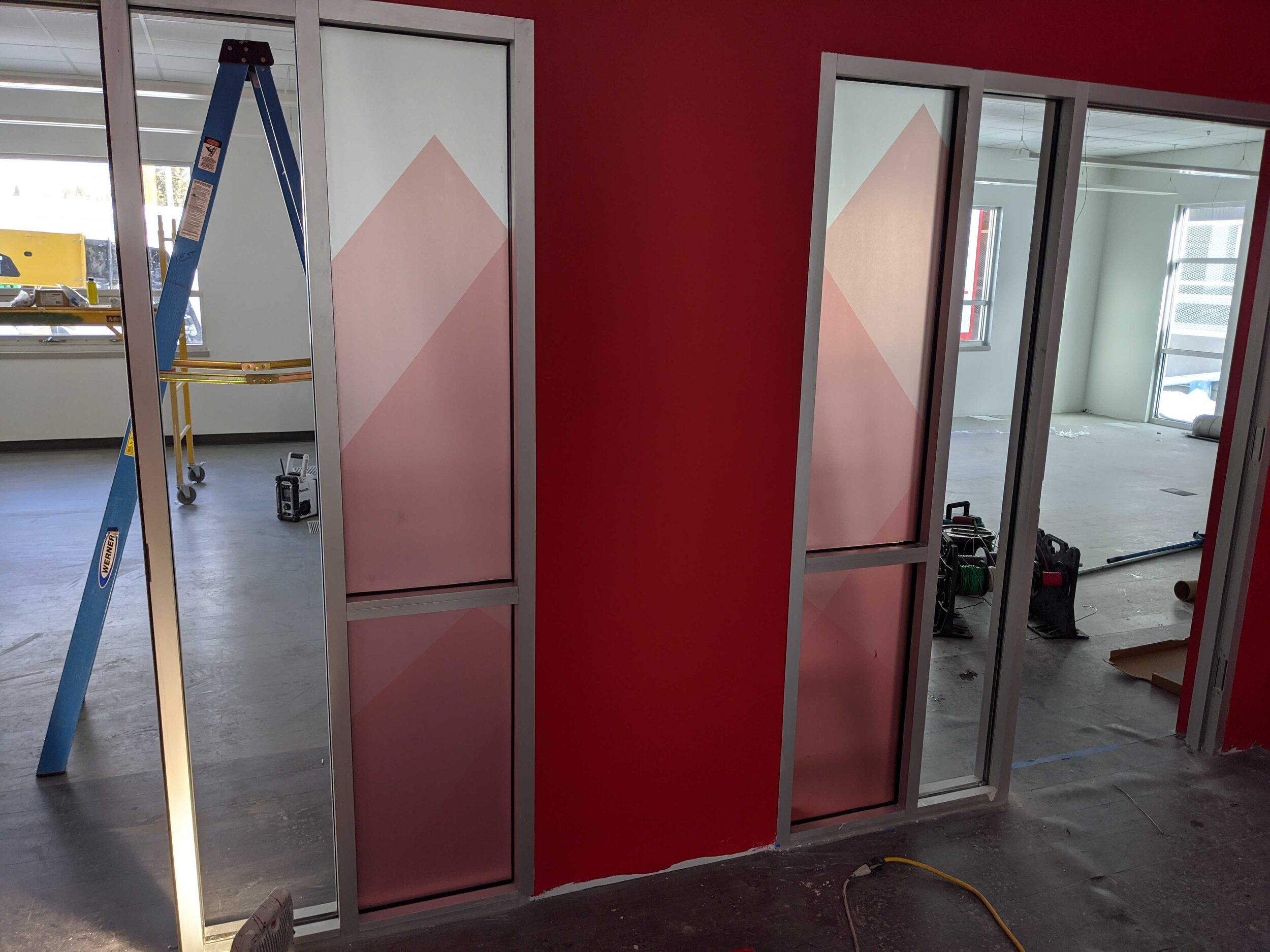 Interior of a room under construction with a red wall featuring two glass doors. Both glass doors have frosted privacy vinyl. In Butte, Montana.