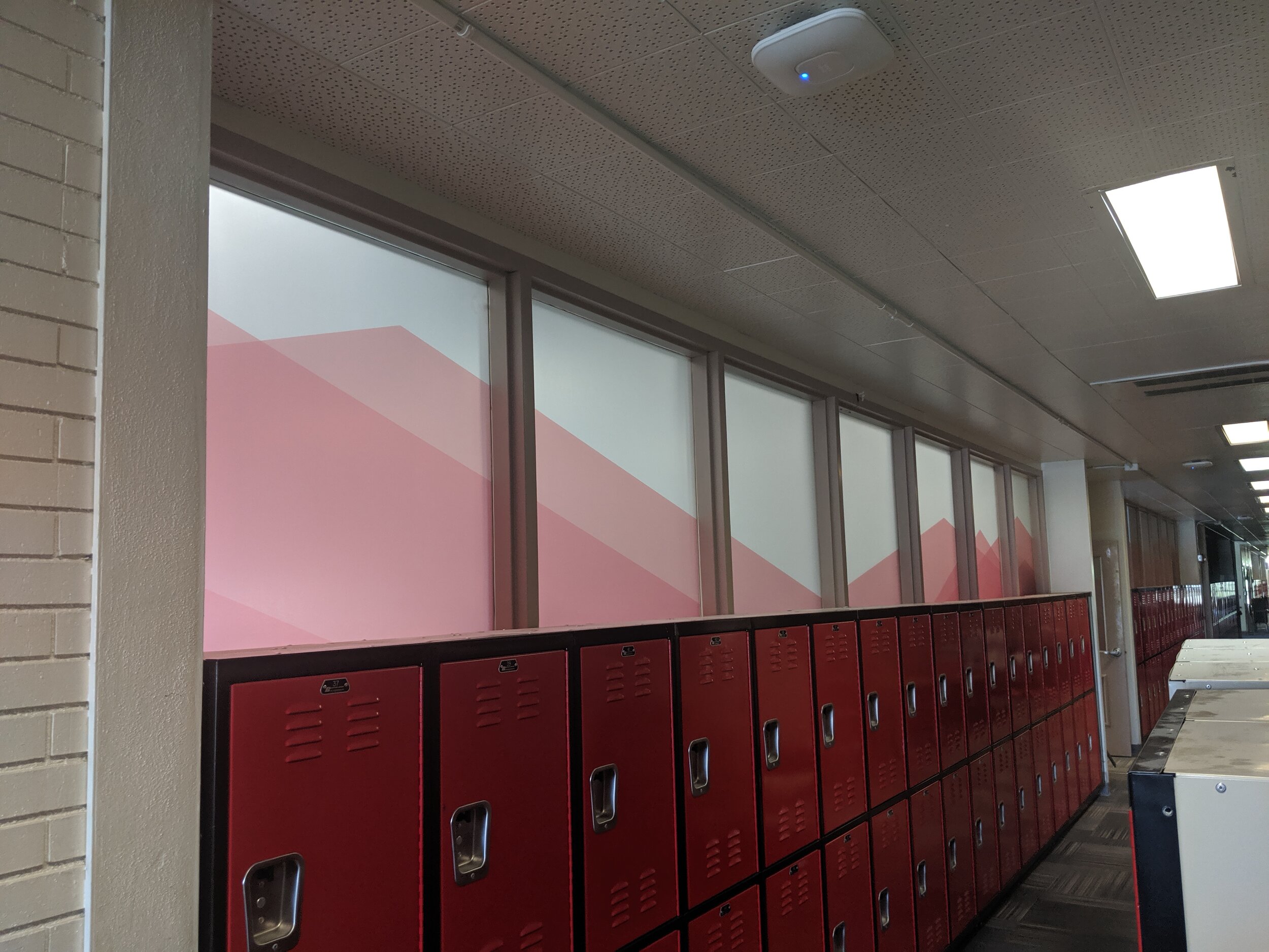 School hallway with red lockers and frosted windows featuring a red geometric design.