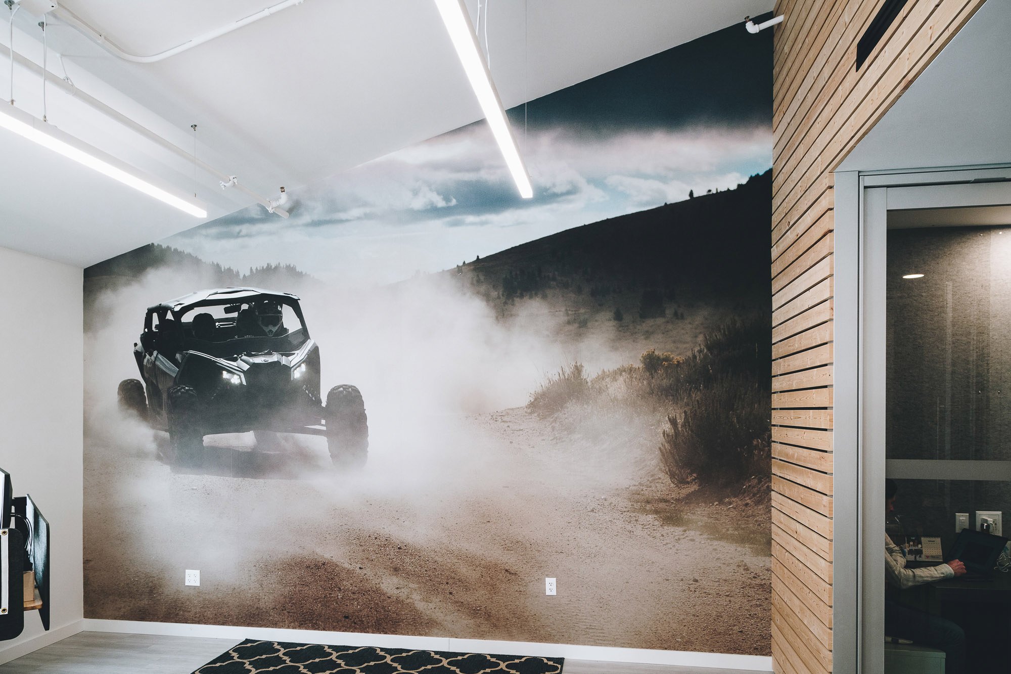 Angled wall wrapped with a photograph of a UTV driving down a dusty trailer with mountains in the background