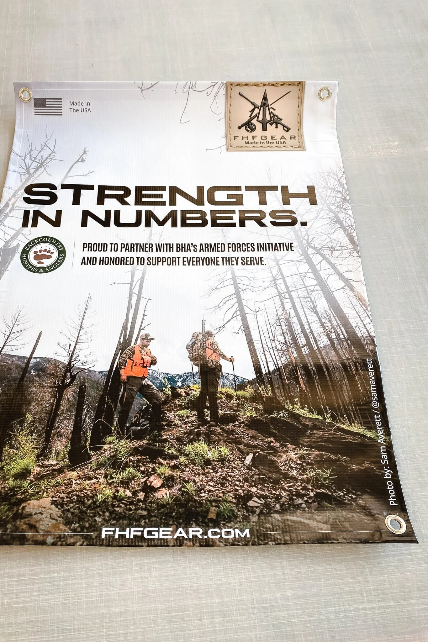 Custom vinyl banner printed for FHF Gear featuring the slogan 'Strength in Numbers' with hunters standing in a rugged outdoor scene.