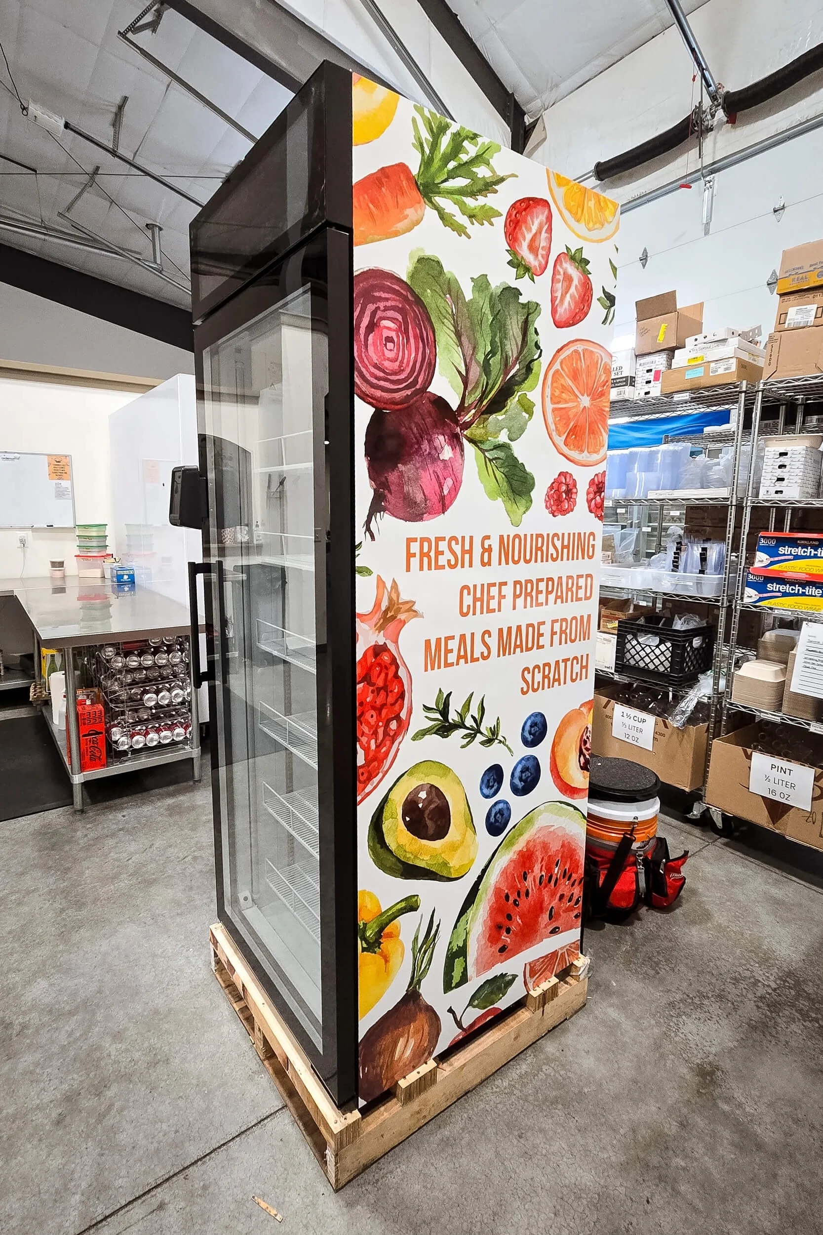 Side panel of a fridge vending machine with a colorful collage of illustrated fruits and vegetables for OrdersUp!