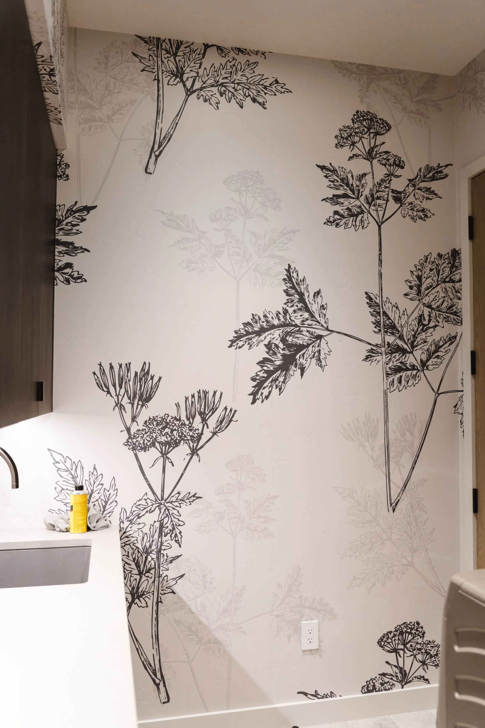 Modern wall wrap featuring oversized black-and-white botanical illustrations on cream walls in a kitchenette or utility room, adding a minimalist nature-inspired touch. Installed at a residential home in Big Sky, MT.