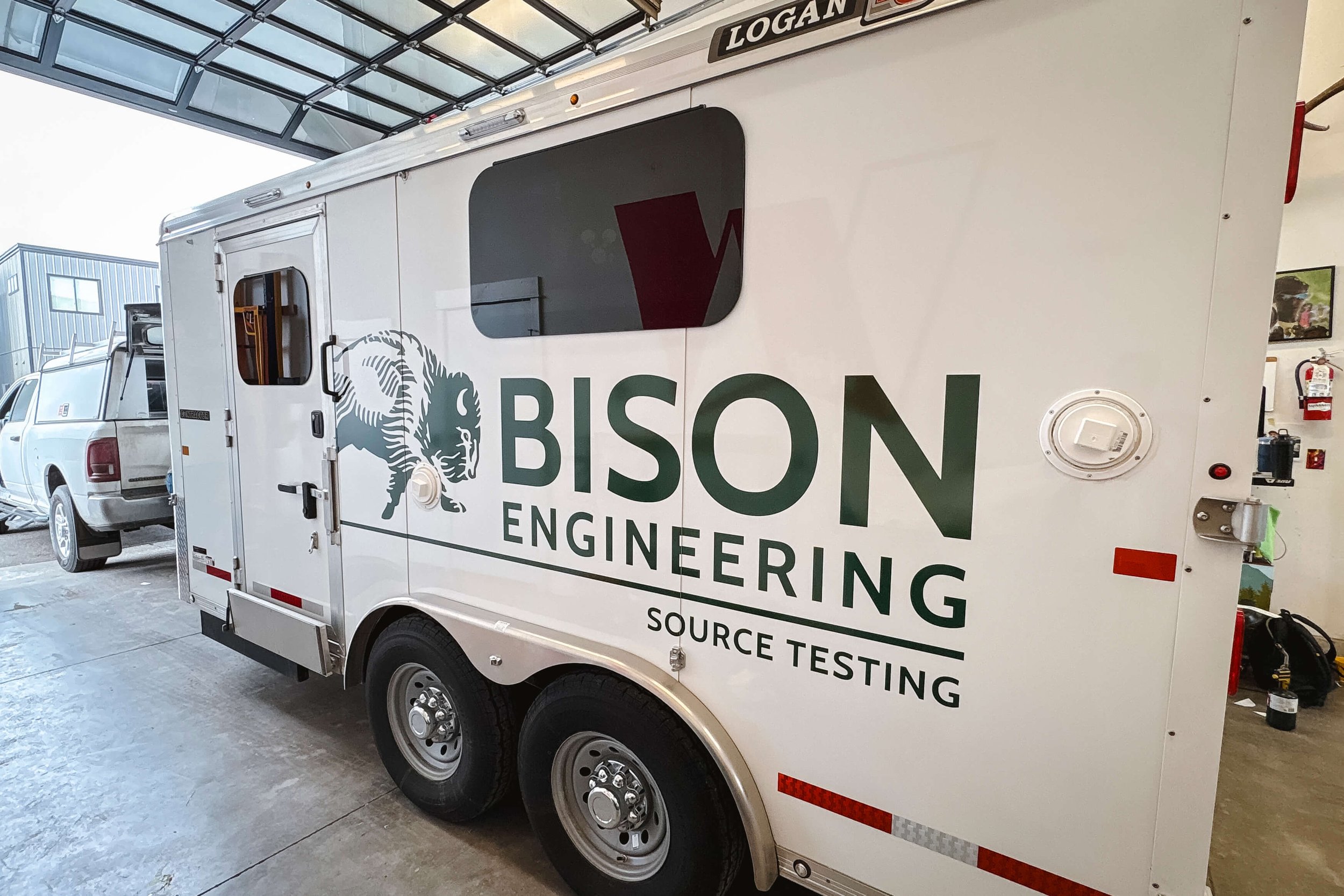Side view of a white trailer with dark green stacked Bison Engineering text beneath a window. An outline illustration of a bison is running towards the text