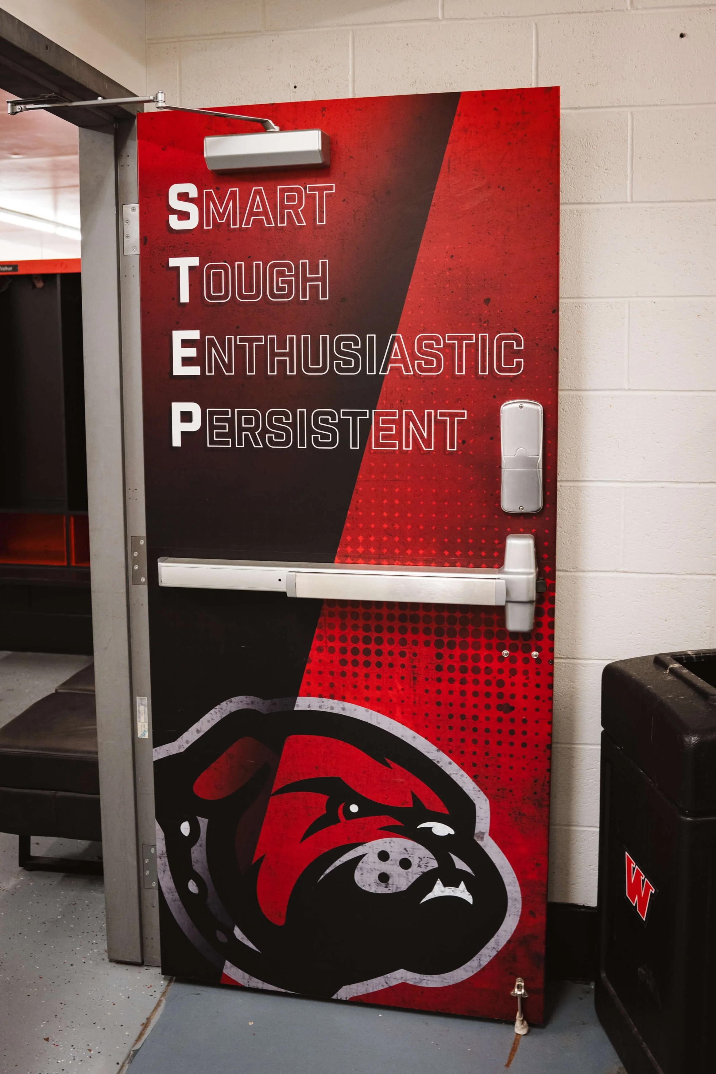 Motivational wall wrap on a door displaying the acronym “STEP – Smart, Tough, Enthusiastic, Persistent” with the Montana Western bulldog logo in red and black tones in Dillon, MT.