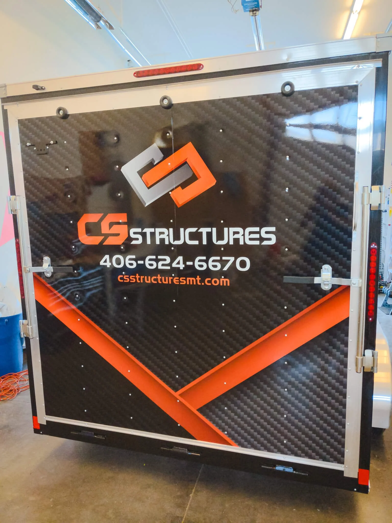 CS Structures trailer wrap in Bozeman, Montana, with high-impact carbon fiber pattern, bold red and gray interlocked logo, and custom lettering promoting construction services and contact info.