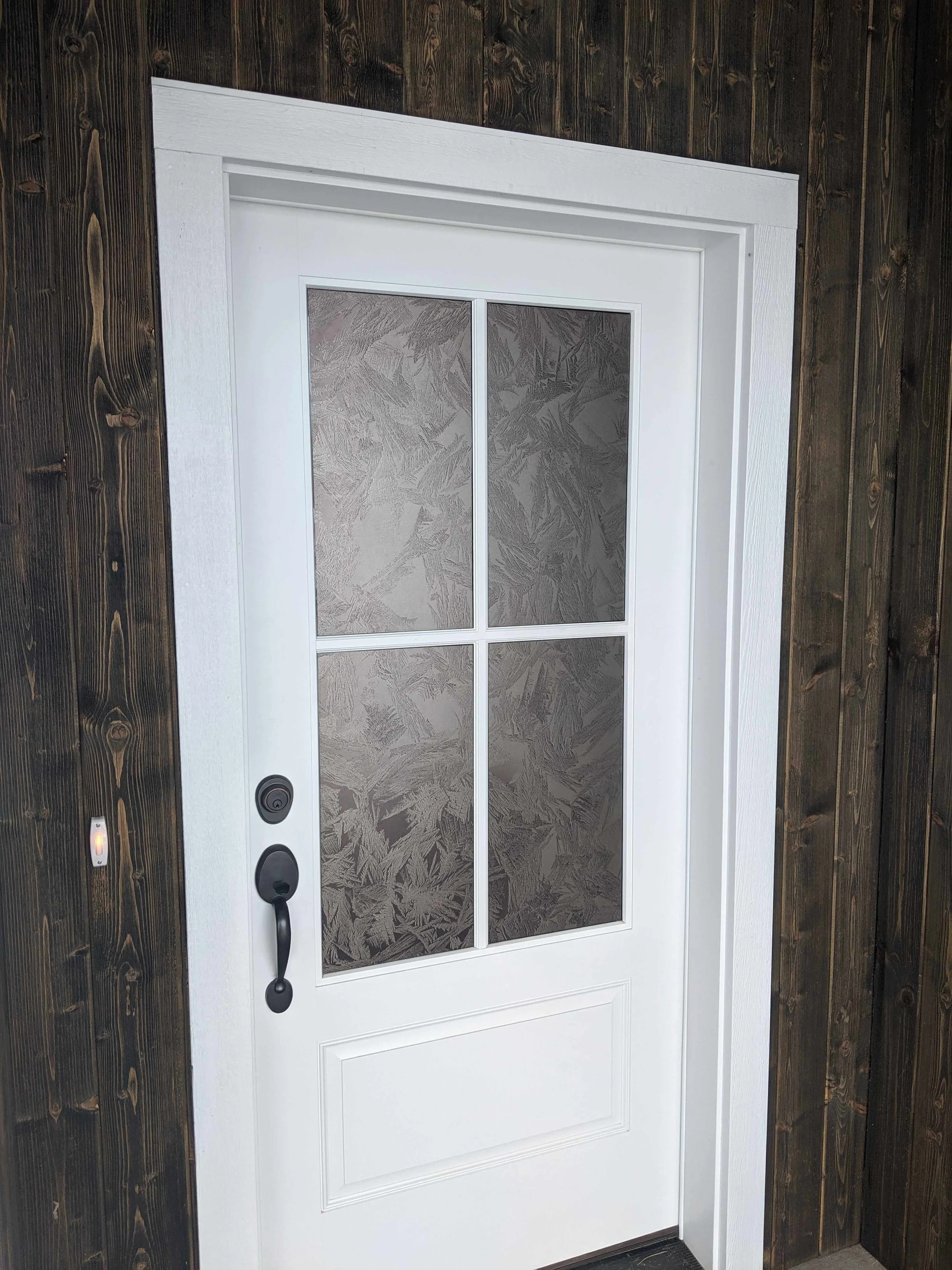 A white exterior door with four glass panes featuring subtle frosted window graphics with a leaf pattern, providing privacy window film while preserving natural light.