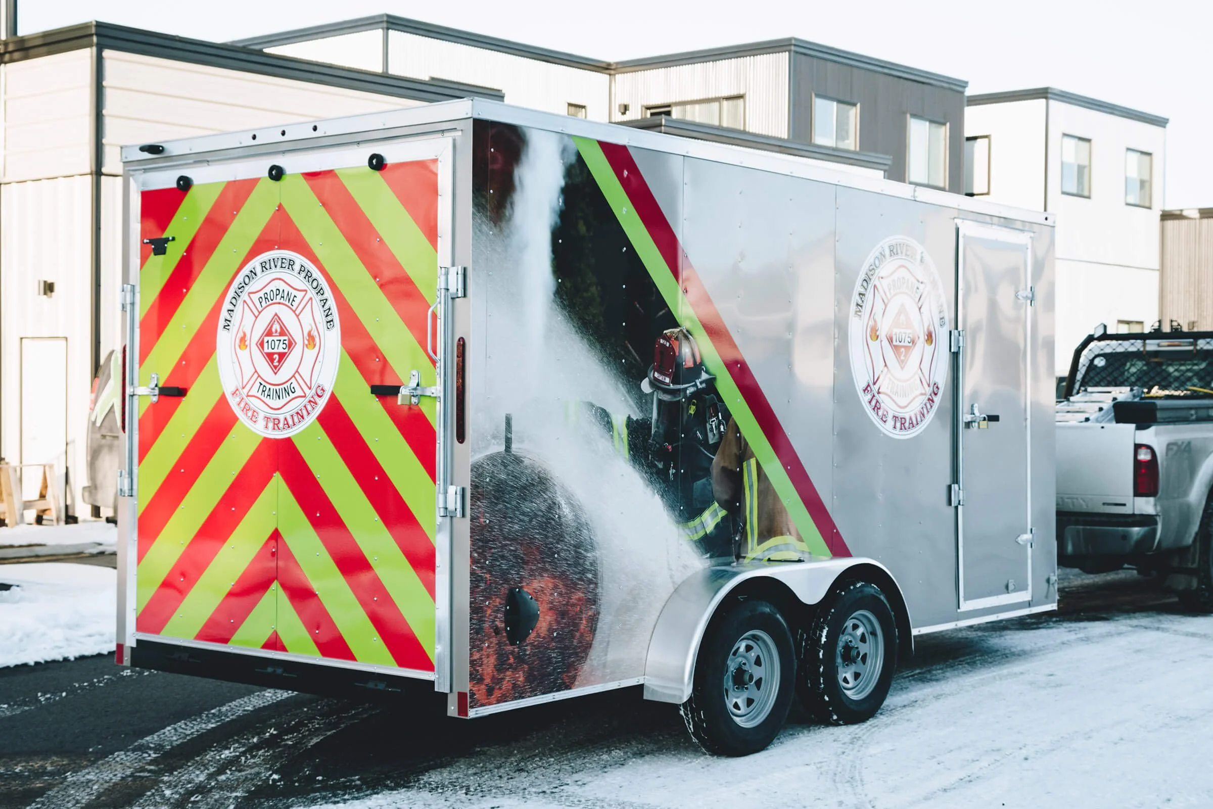 High-visibility trailer wrap for Madison River Propane Fire Training in Bozeman, Montana, featuring diagonal red and green safety stripes and a firefighter mid-action graphic.