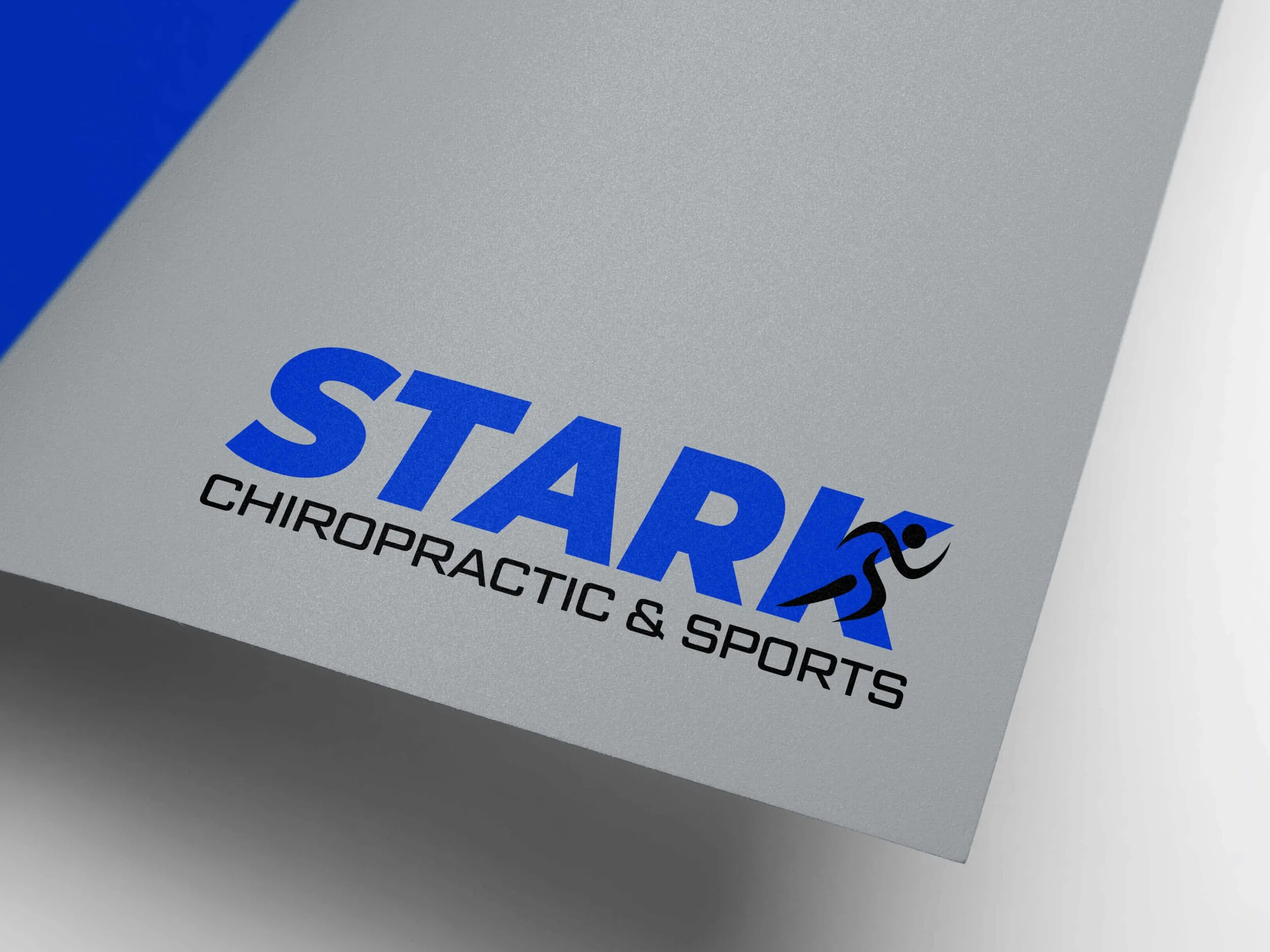 Stark Chiropractic & Sports logo on a gray surface with blue and black text, featuring a stylized running figure within the letter K.