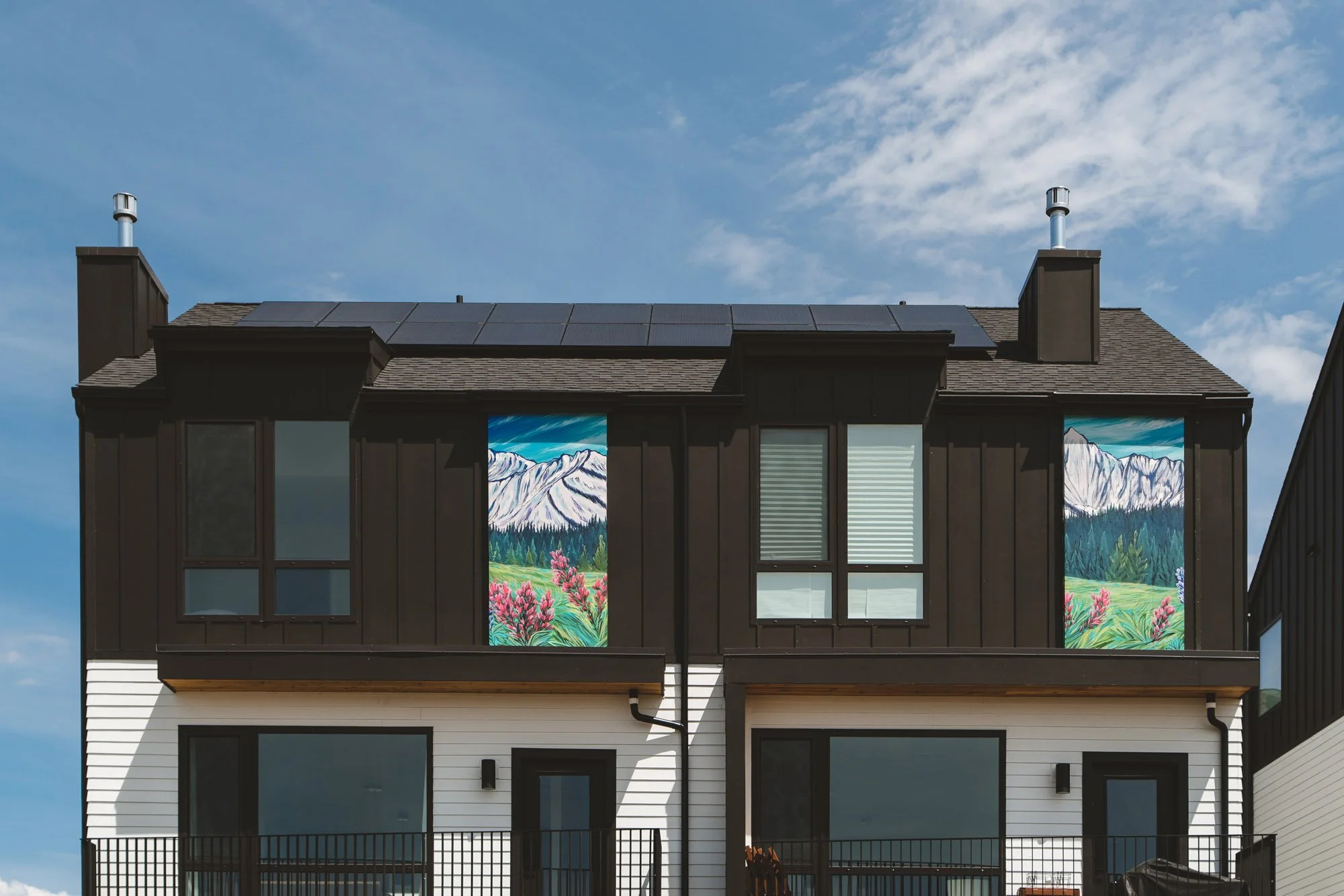 Townhome exteriors featuring scenic mountain and wildflower mural wall wraps integrated between windows for an artistic architectural accent in Bozeman, MT.