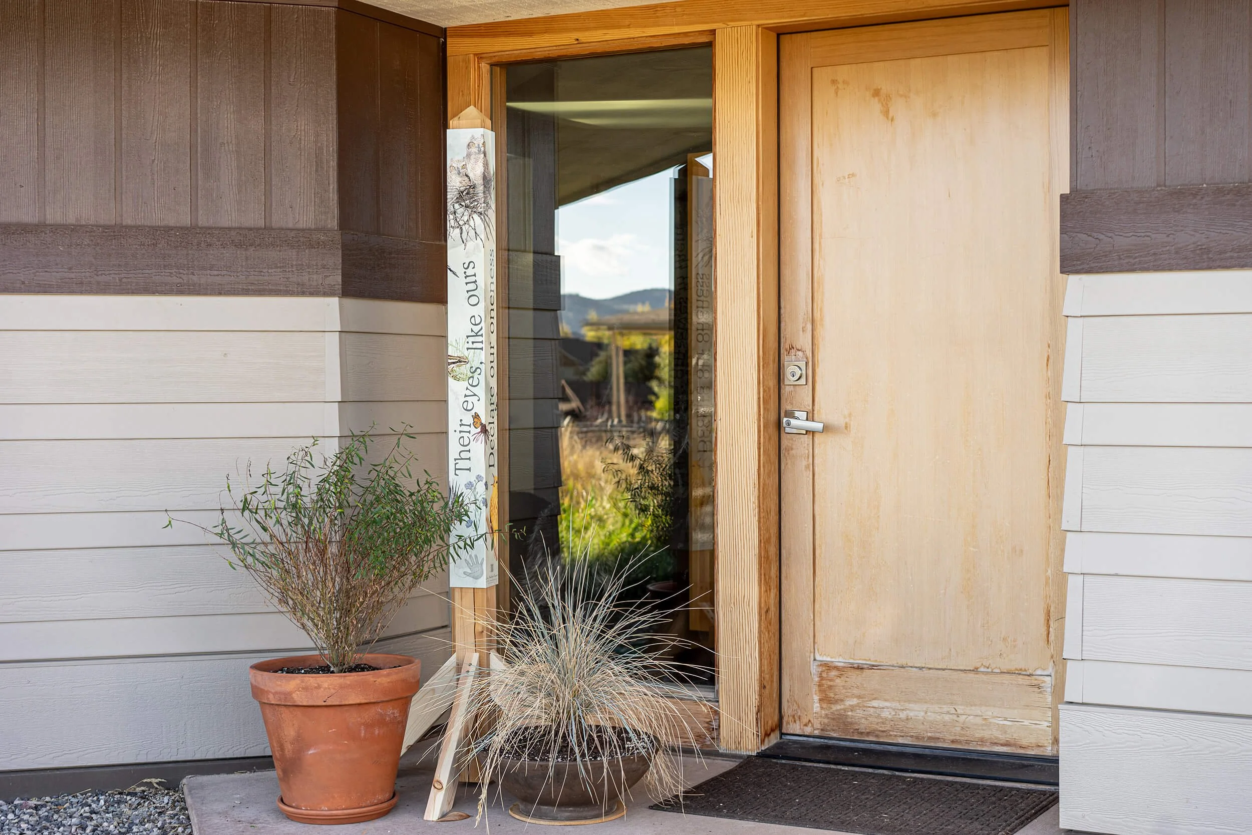 Custom vinyl wrap on a tall vertical wooden post featuring minimalist illustrations and the phrase “Their eyes, like ours,” used as an entry accent at a residential doorway.