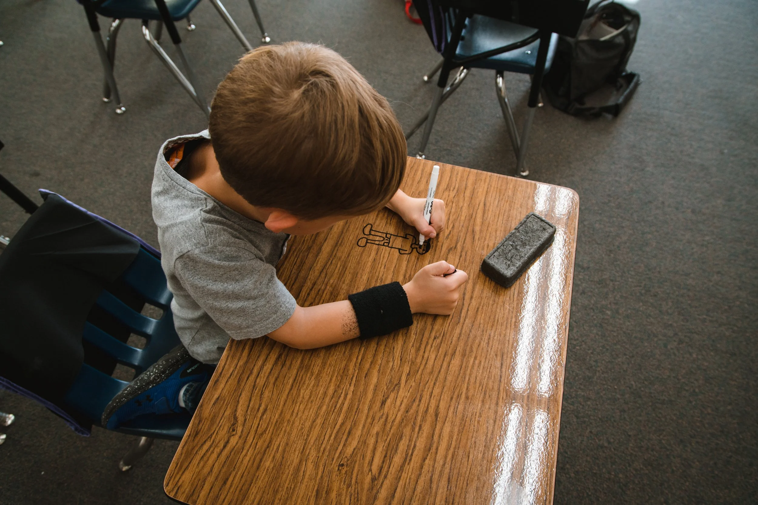 Overhead view of a student drawing on a dry erase desktop beside a rectangular eraser.