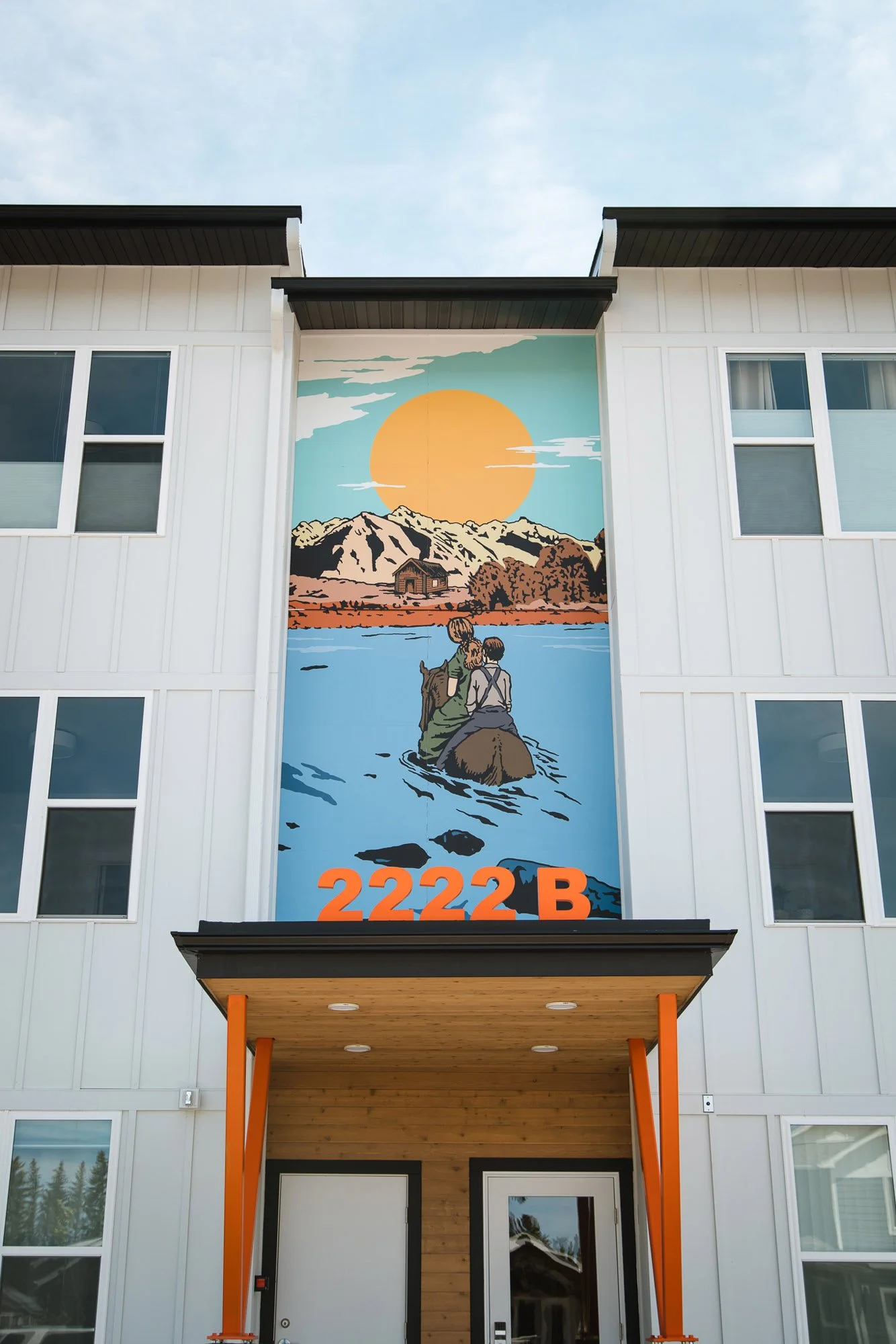 Vibrant outdoor wall wrap above a townhouse entrance depicting two figures canoeing on a lake with mountains and a sunset, labeled “2222B” in Bozeman, MT.