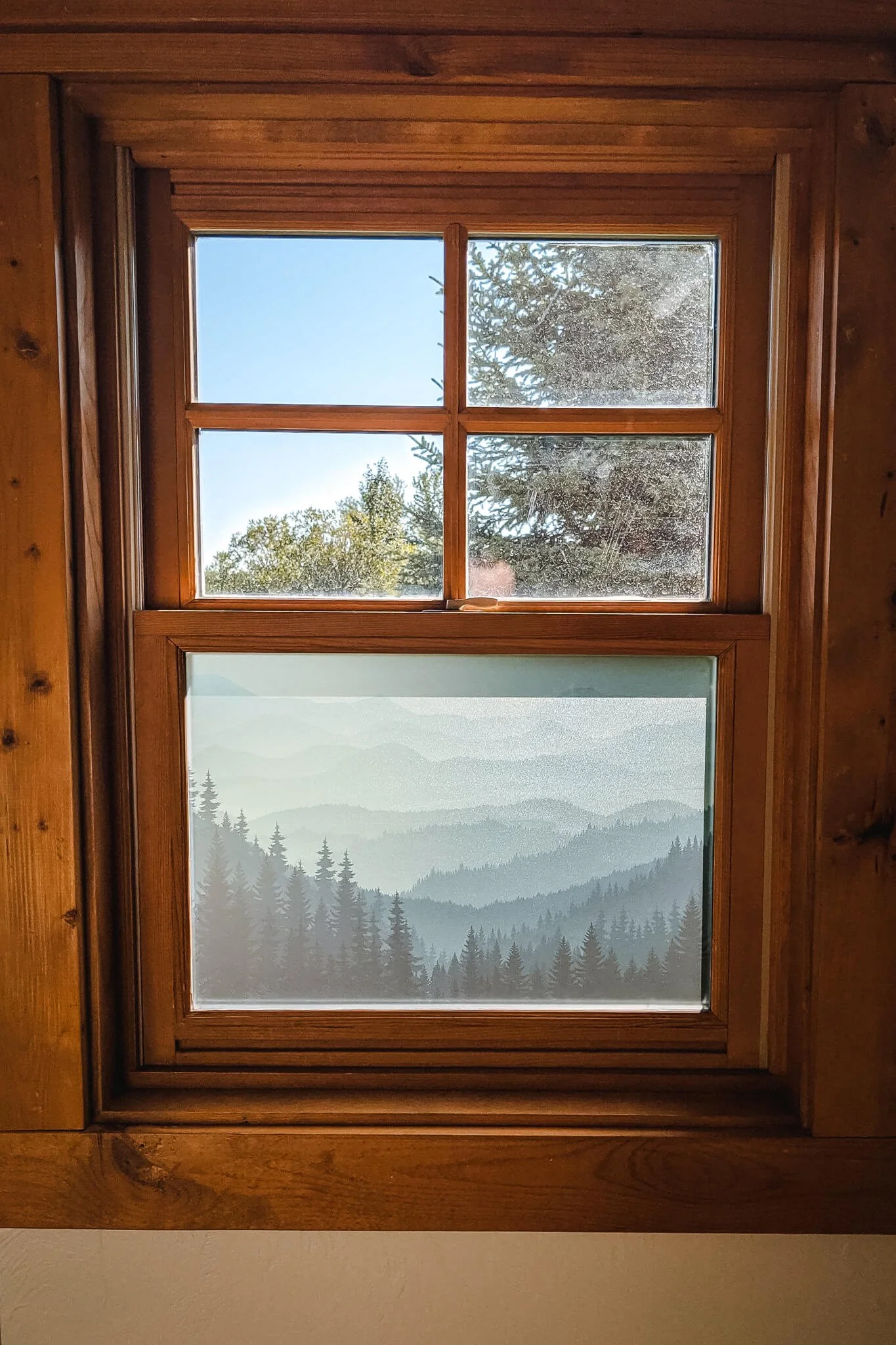 Rustic interior window features a detailed forest and mountain design printed on the lower pane as a decorative privacy window graphic.