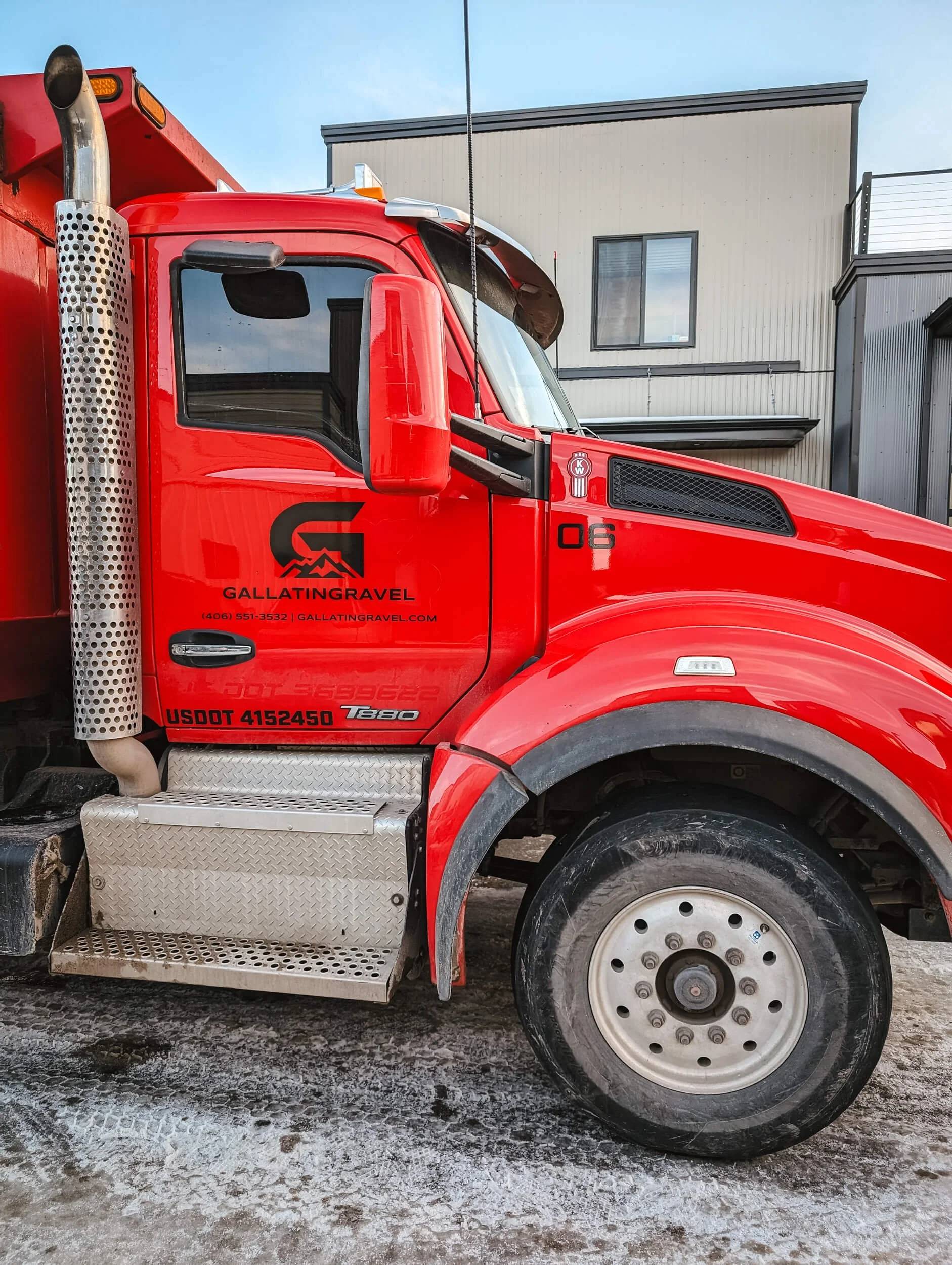 Gallatin Gravel red dump truck in Bozeman, Montana, with bold black logo and USDOT number displayed on the door, showcasing custom vinyl vehicle wraps designed for heavy-duty branding needs.